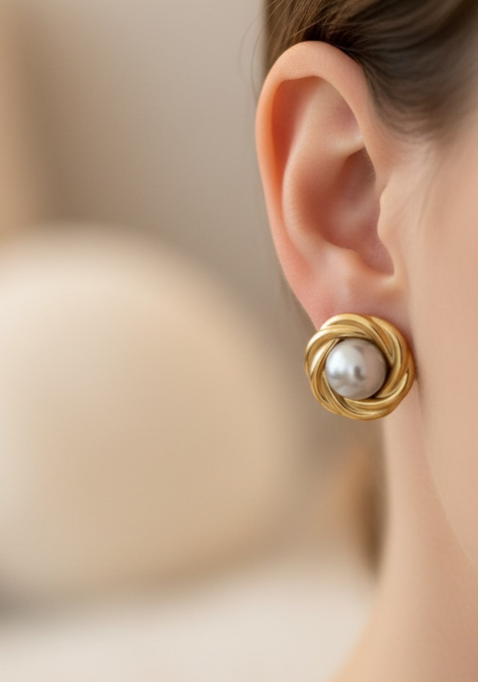 Gold earring with a pearl on an ear against a blurred background