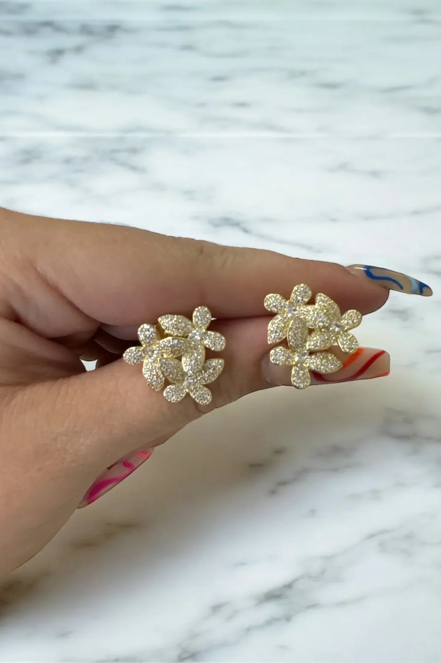 The earrings held up by a hand model.