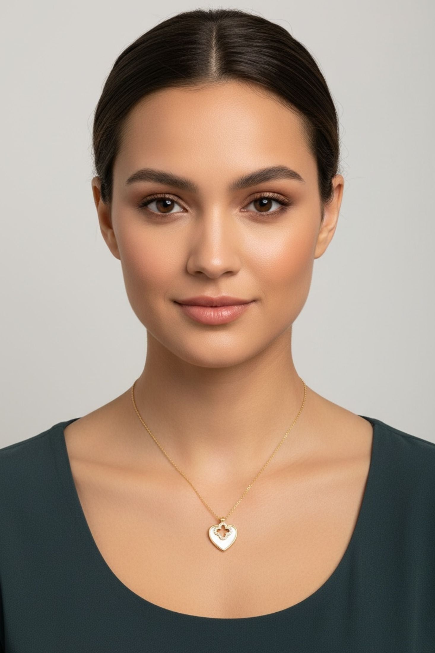 Woman wearing a gold necklace with a heart pendant against a neutral background