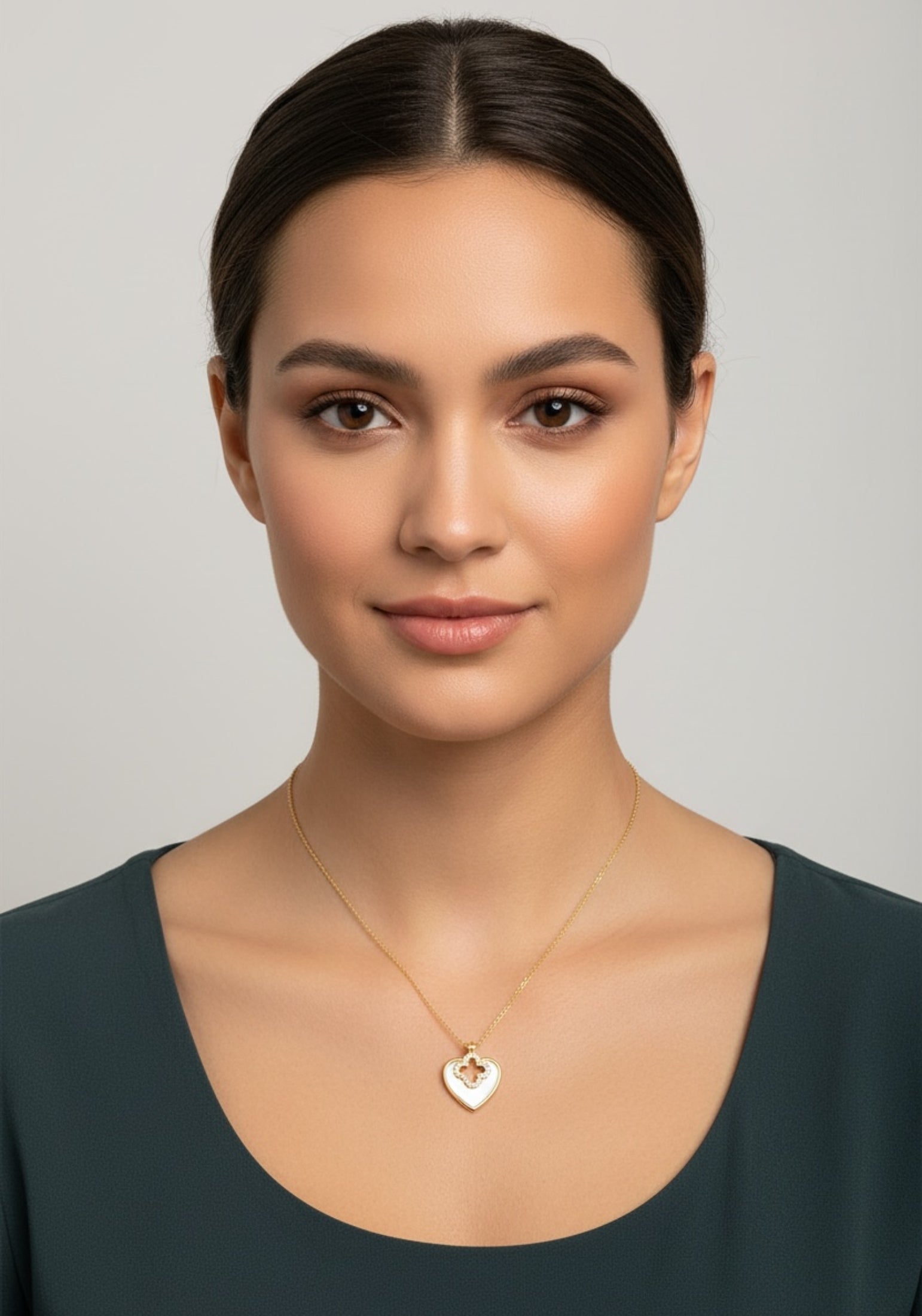 Woman wearing a gold necklace with a heart pendant against a neutral background