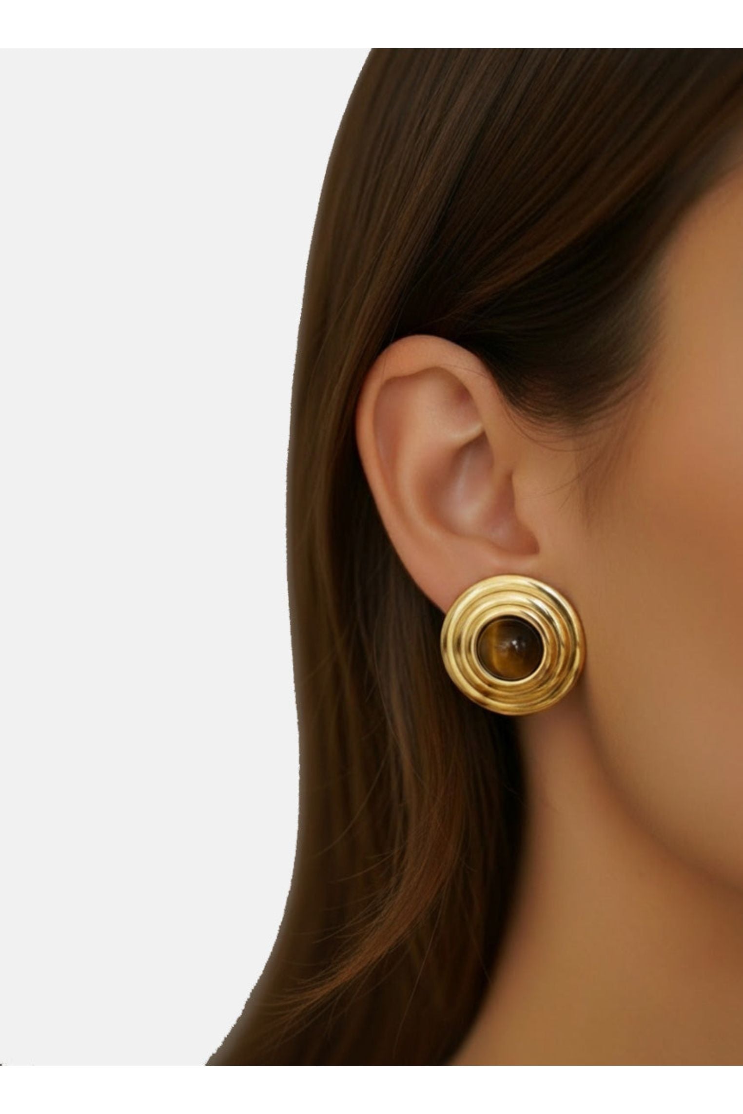 Gold earring worn by a person with a plain background