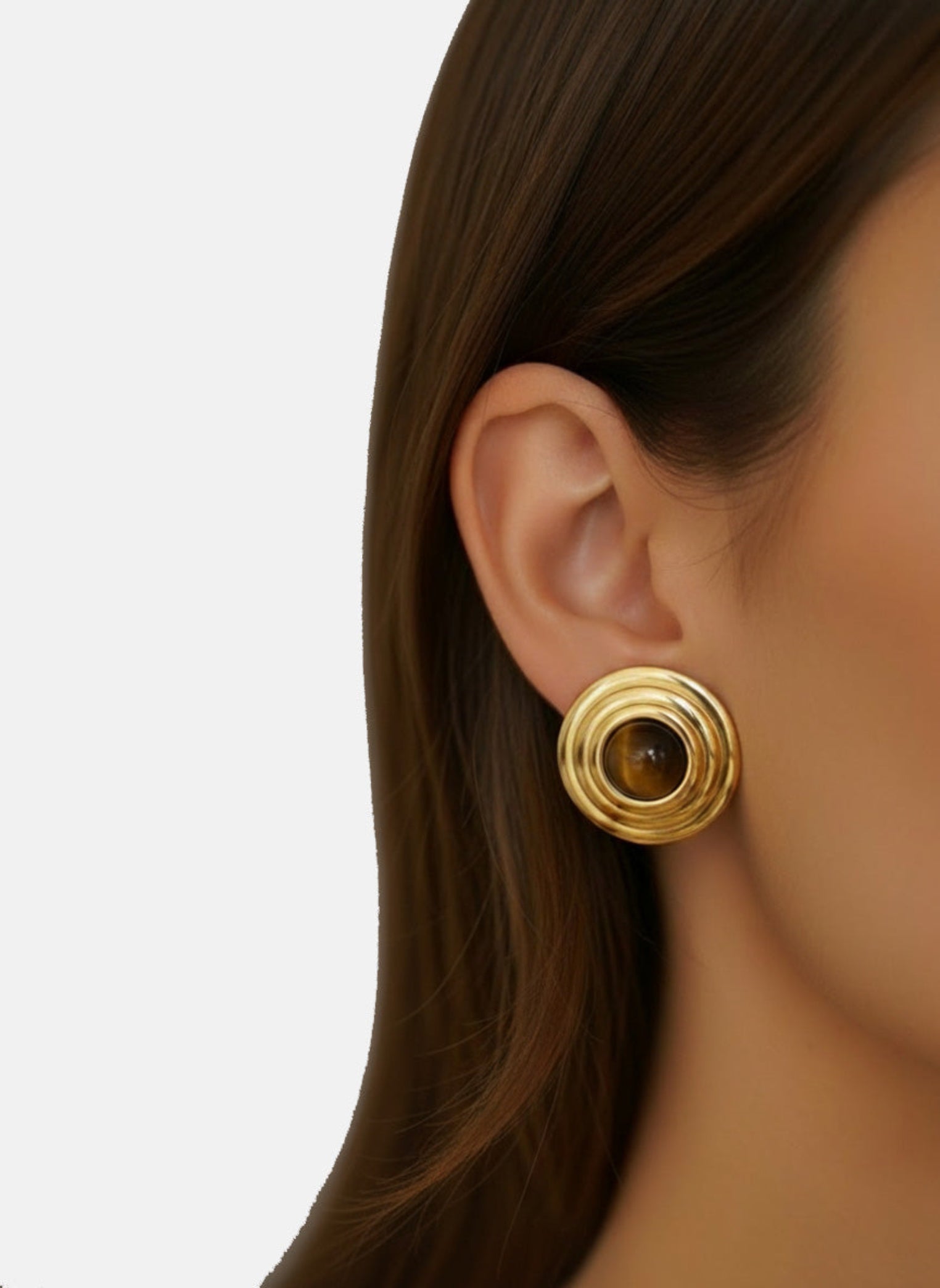 Gold earring worn by a person with a plain background