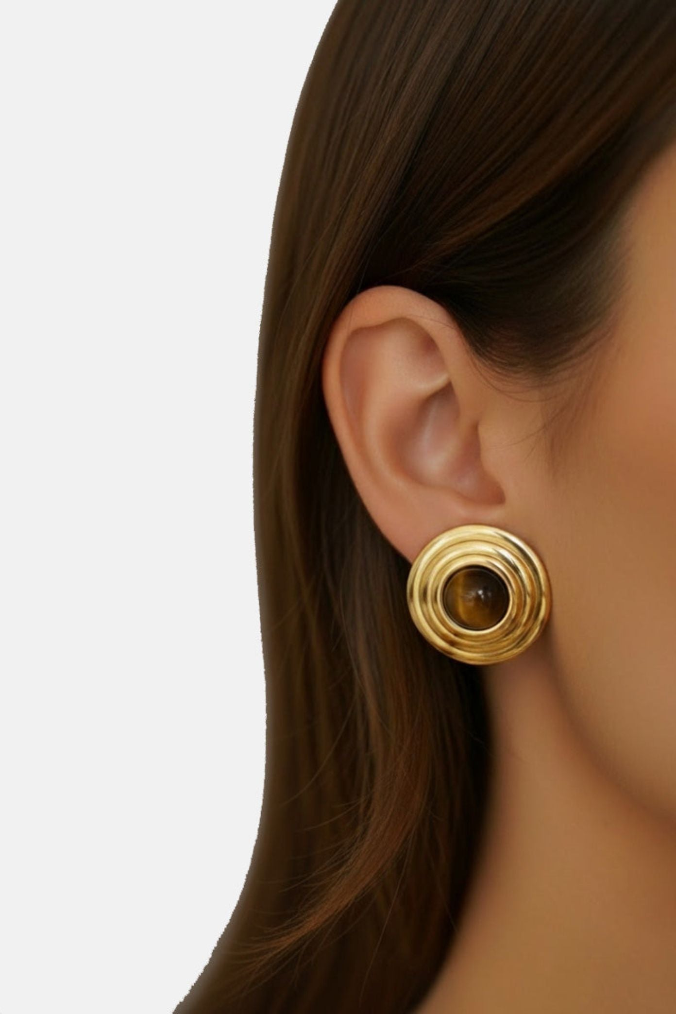Gold earring worn by a person with a plain background