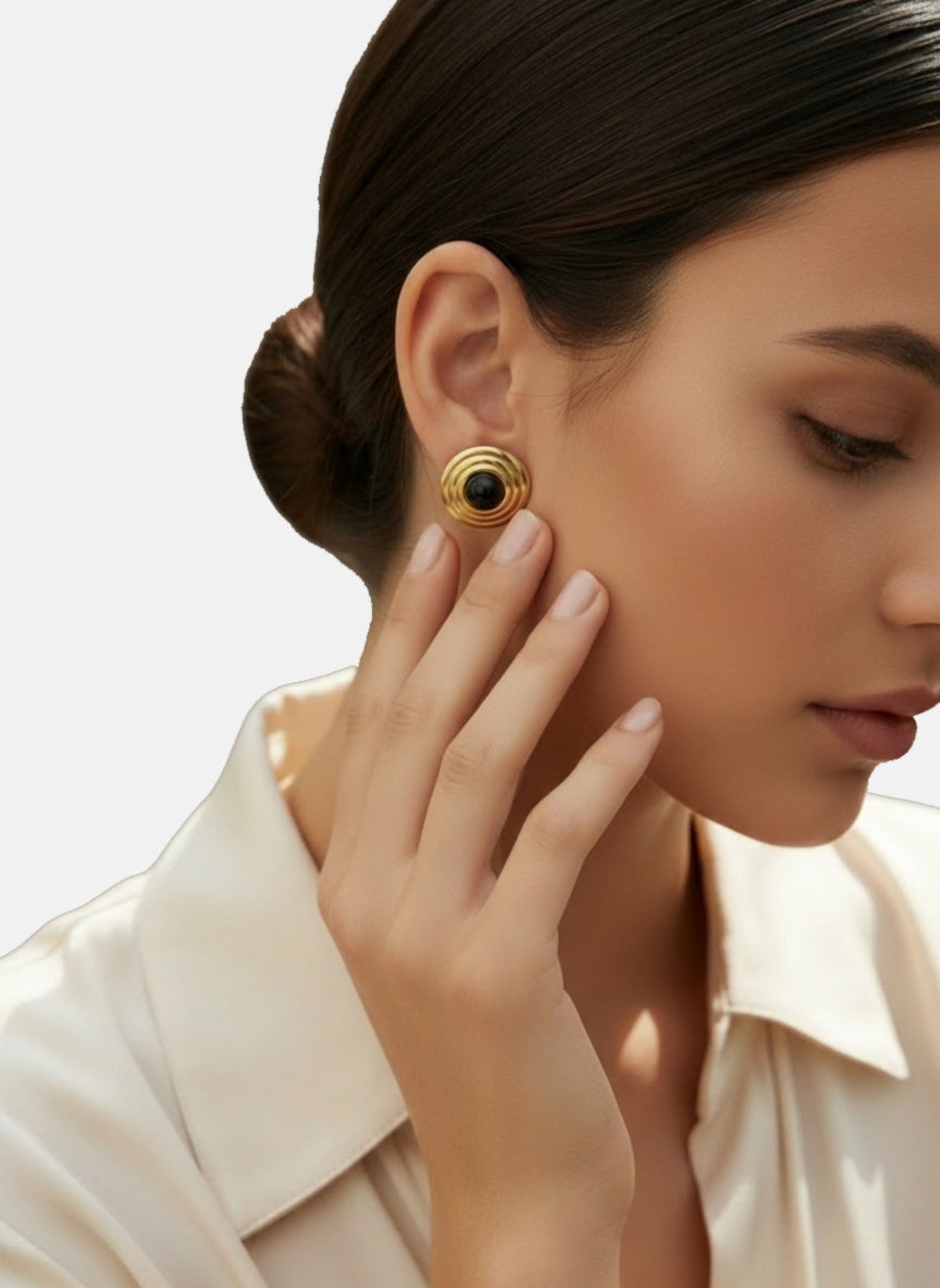 Close-up of a woman wearing gold earrings with a black gemstone on a neutral background