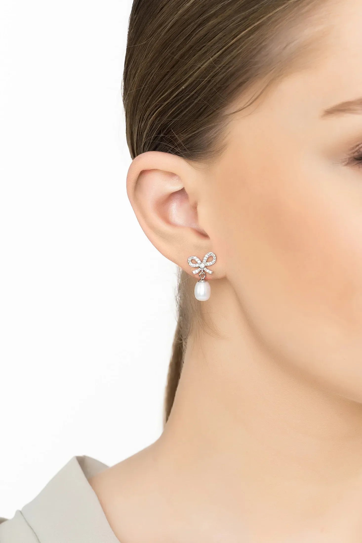 Angled view of Petite Bow Pearl Drop Earrings Silver, showing bow design, pearl detailing, silver finish and the jewellery profile.