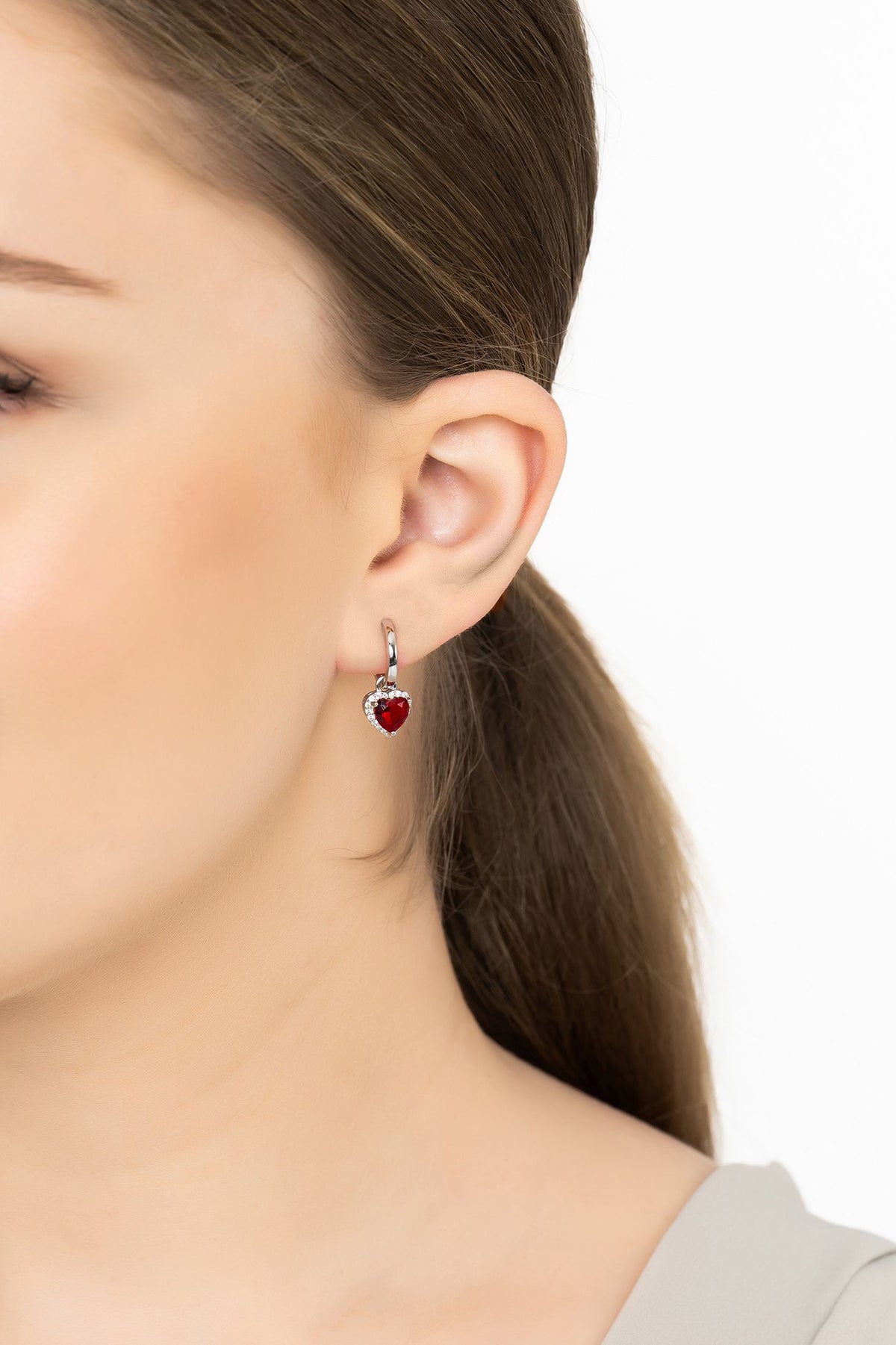 Angled view of Cupids Sparkle Ruby Heart Drop Earrings Silver, showing heart design, ruby detailing, silver finish and the jewellery profile.