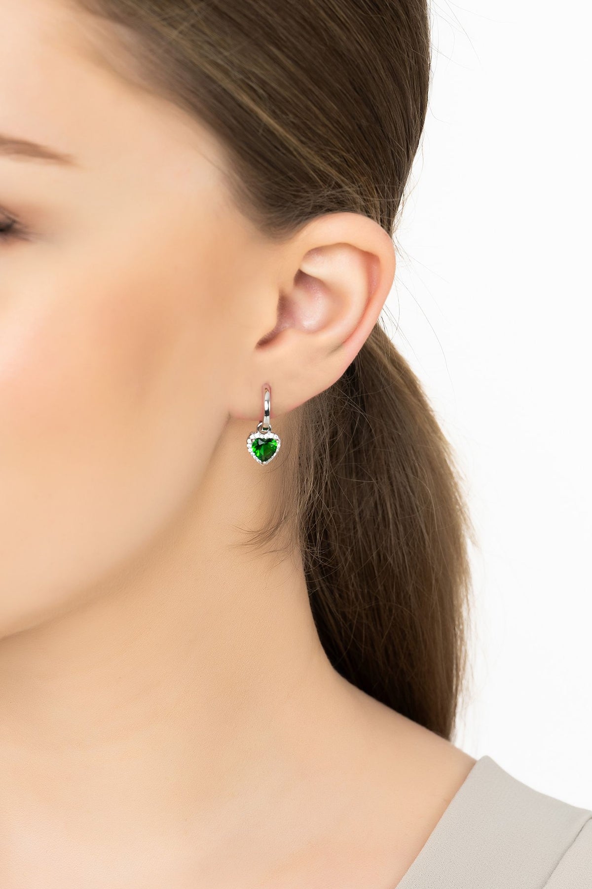 Angled view of Cupids Sparkle Emerald Heart Drop Earrings Silver, showing heart design, emerald detailing, silver finish and the jewellery profile.