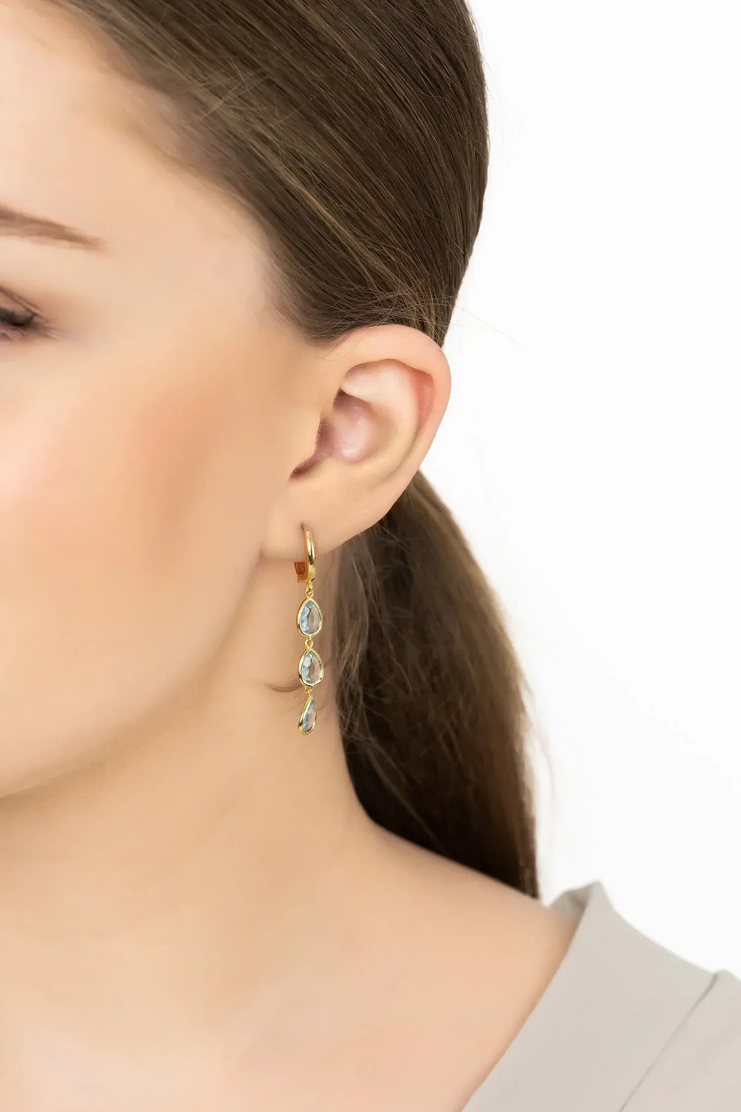 Angled view of Sardinia Triple Teardrop Earrings Gold Blue Topaz, showing blue topaz detailing, gold finish and the jewellery profile.