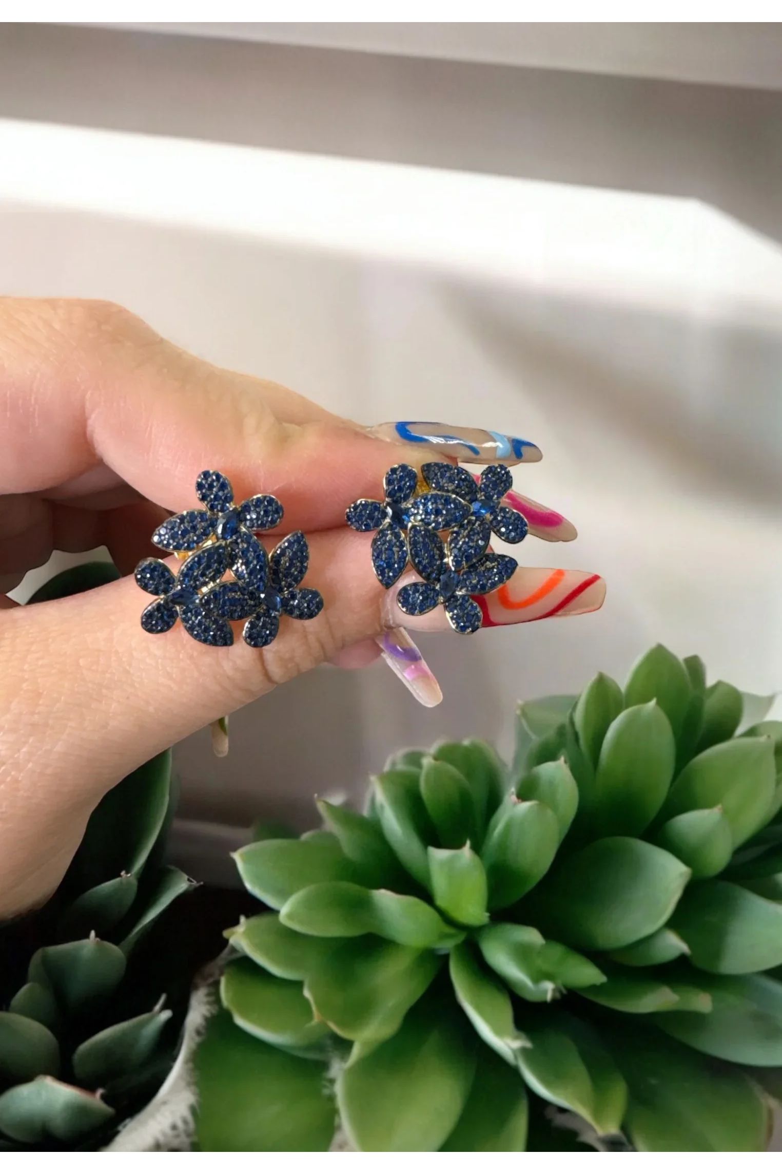 The earrings held up by a hand model.