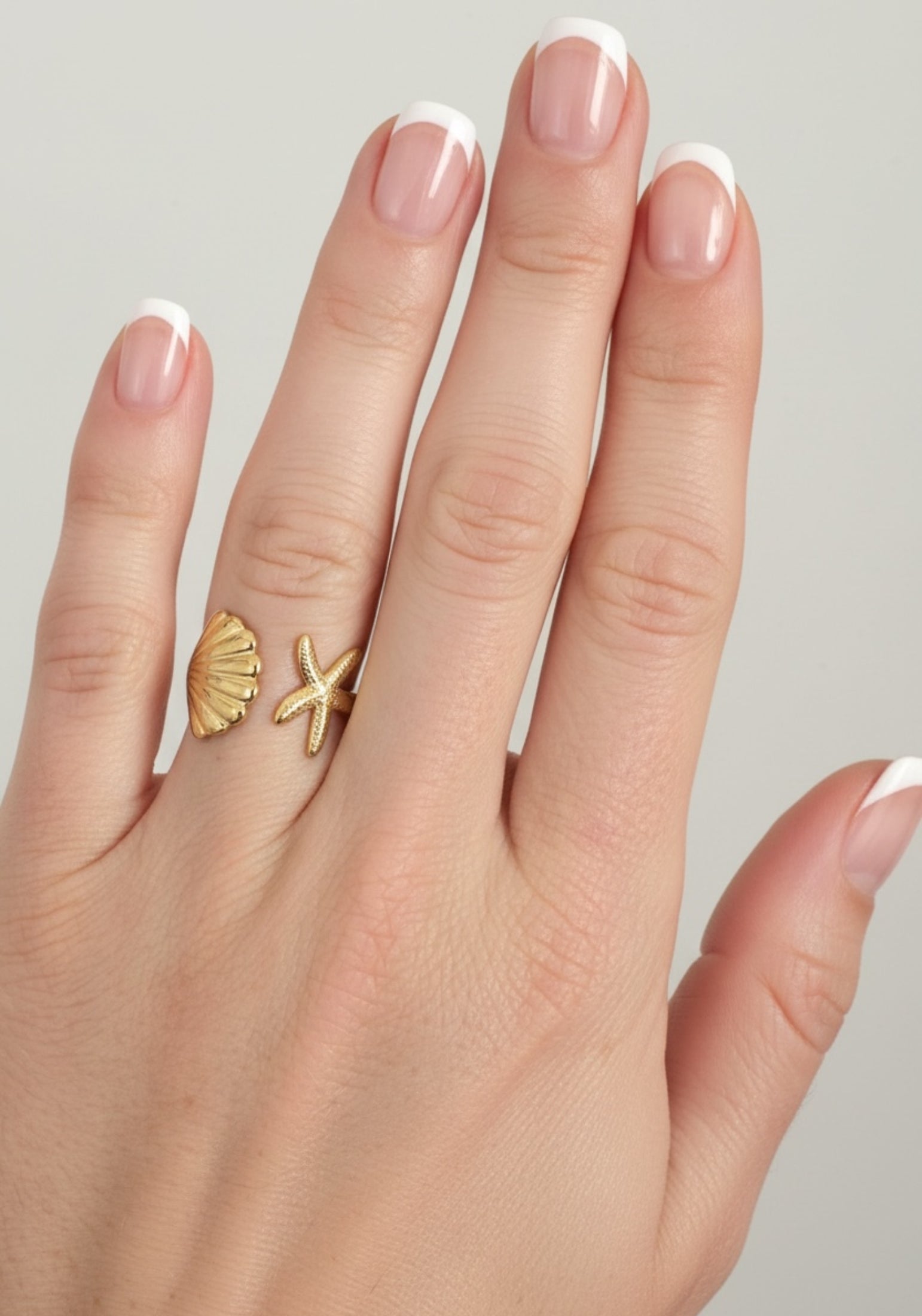 Hand wearing a gold ring with shell and starfish designs on a neutral background