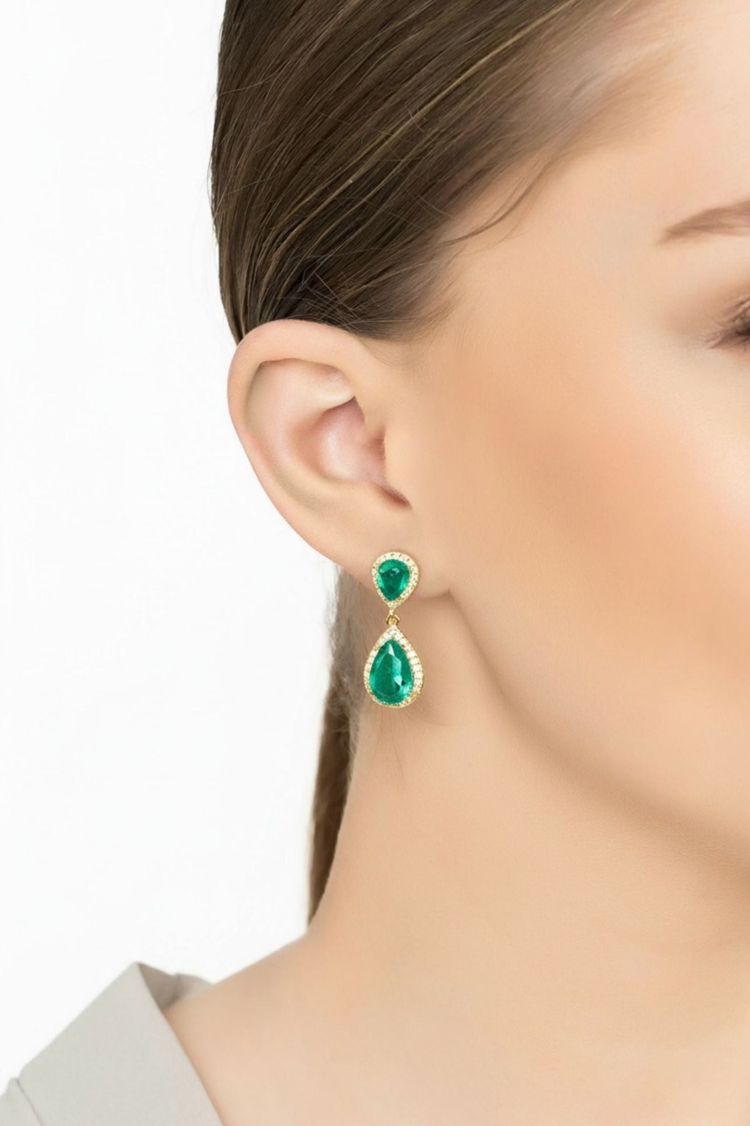 Close-up of a person wearing green teardrop earrings with a plain background