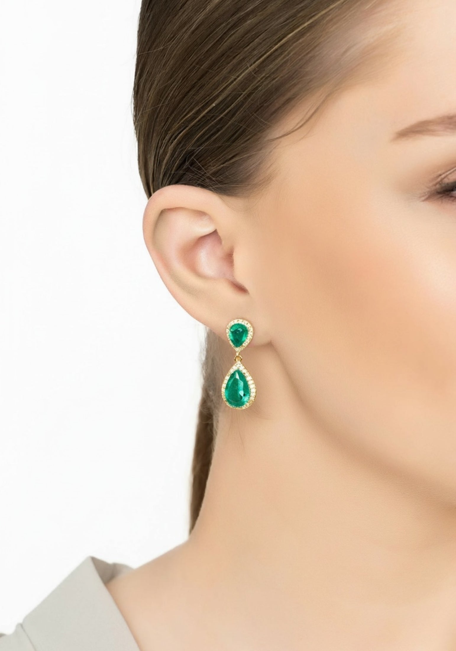 Close-up of a person wearing green teardrop earrings with a plain background