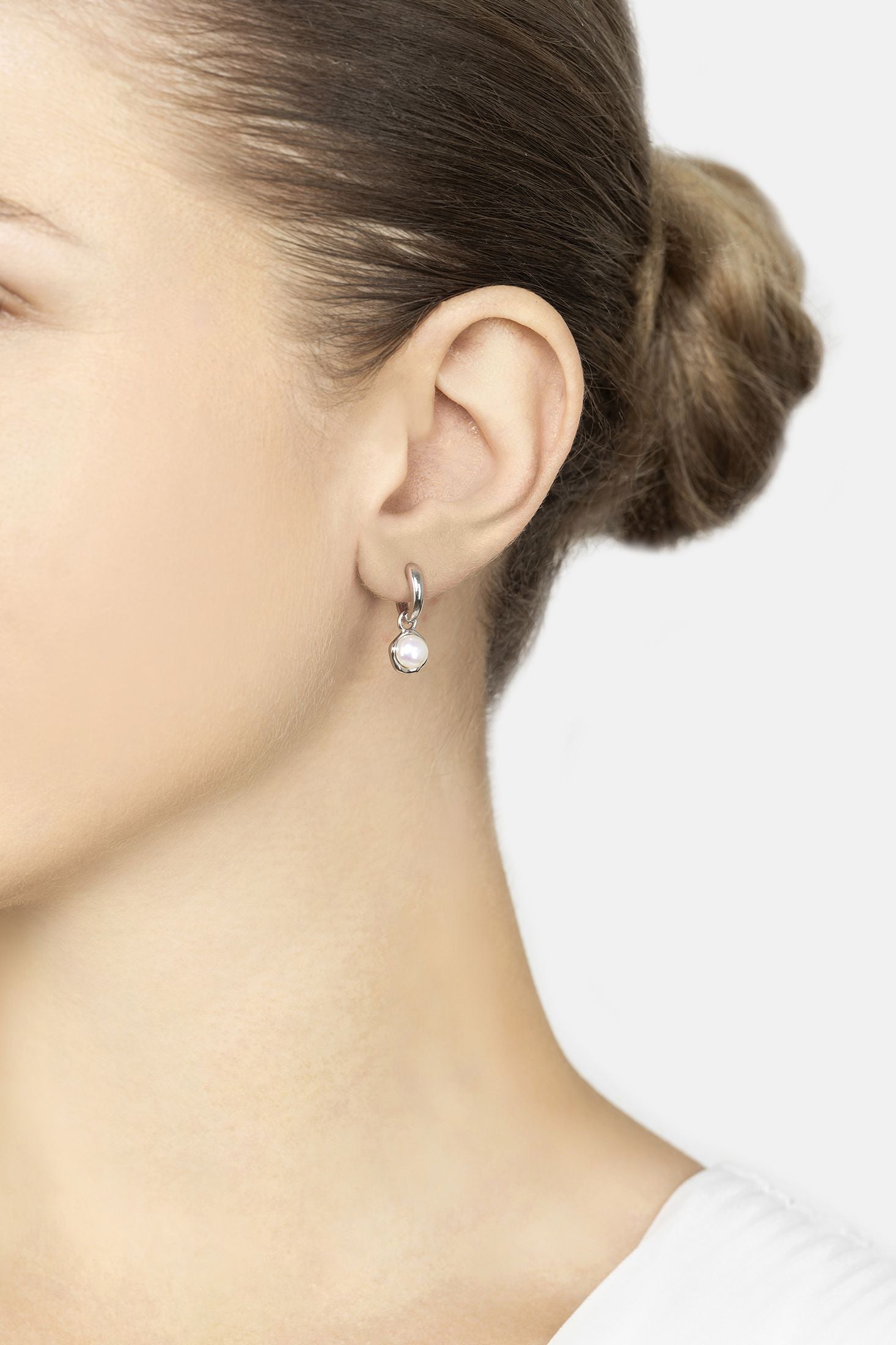 Close-up of a person wearing a silver earring with a pearl on a white background