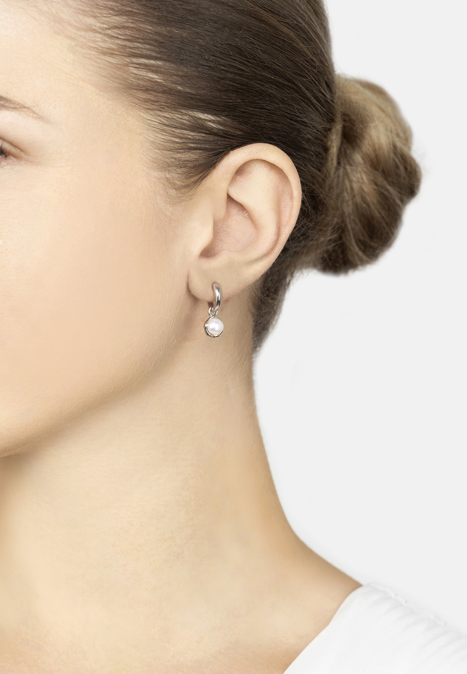 Close-up of a person wearing a silver earring with a pearl on a white background