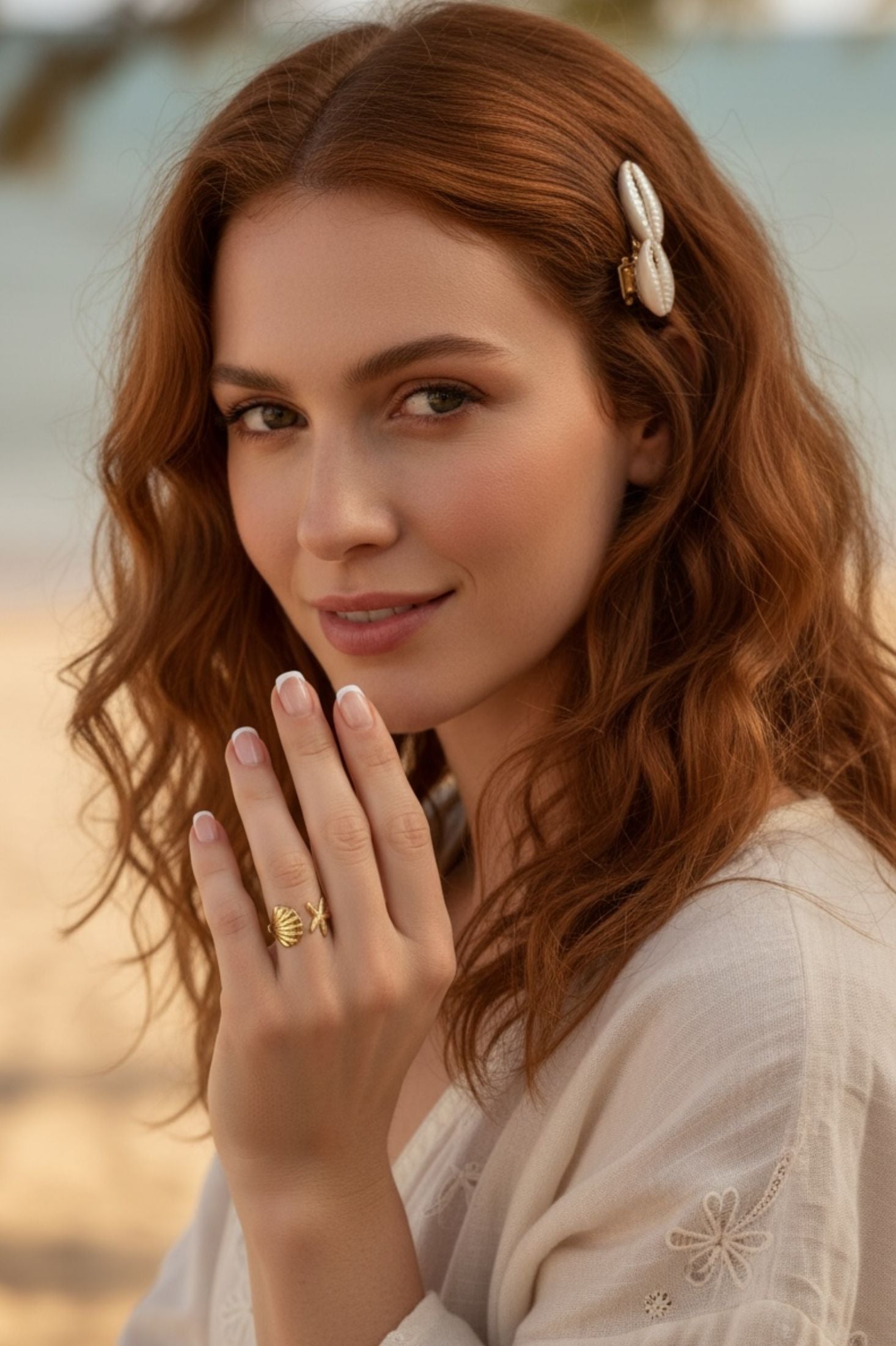 Woman with red hair wearing a gold ring on a blurred beach background