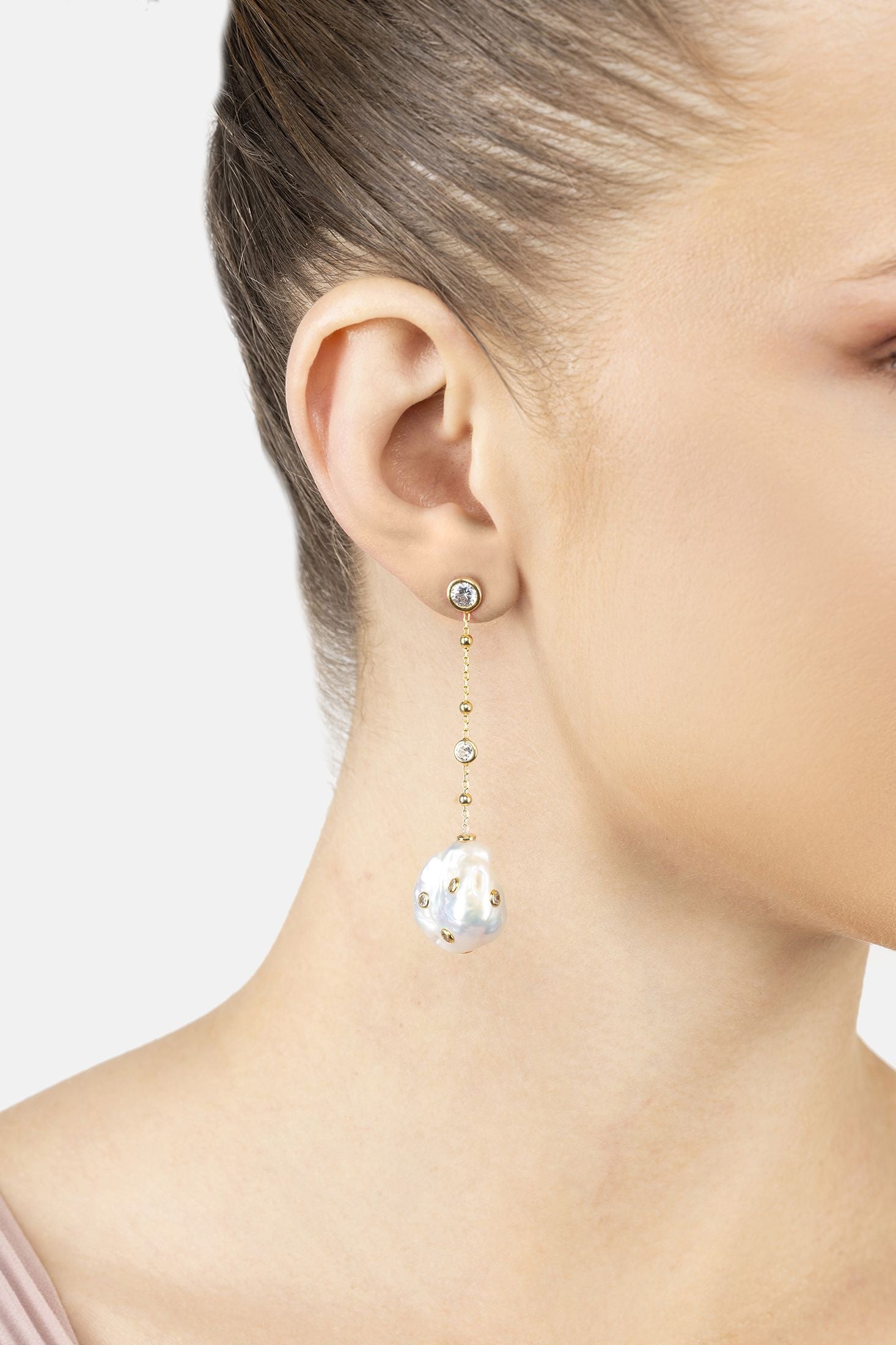 Angled view of Polka Dot Baroque Pearl Chain Drop Earrings Gold Cz, showing baroque pearl and pearl detailing, gold finish and the jewellery profile.