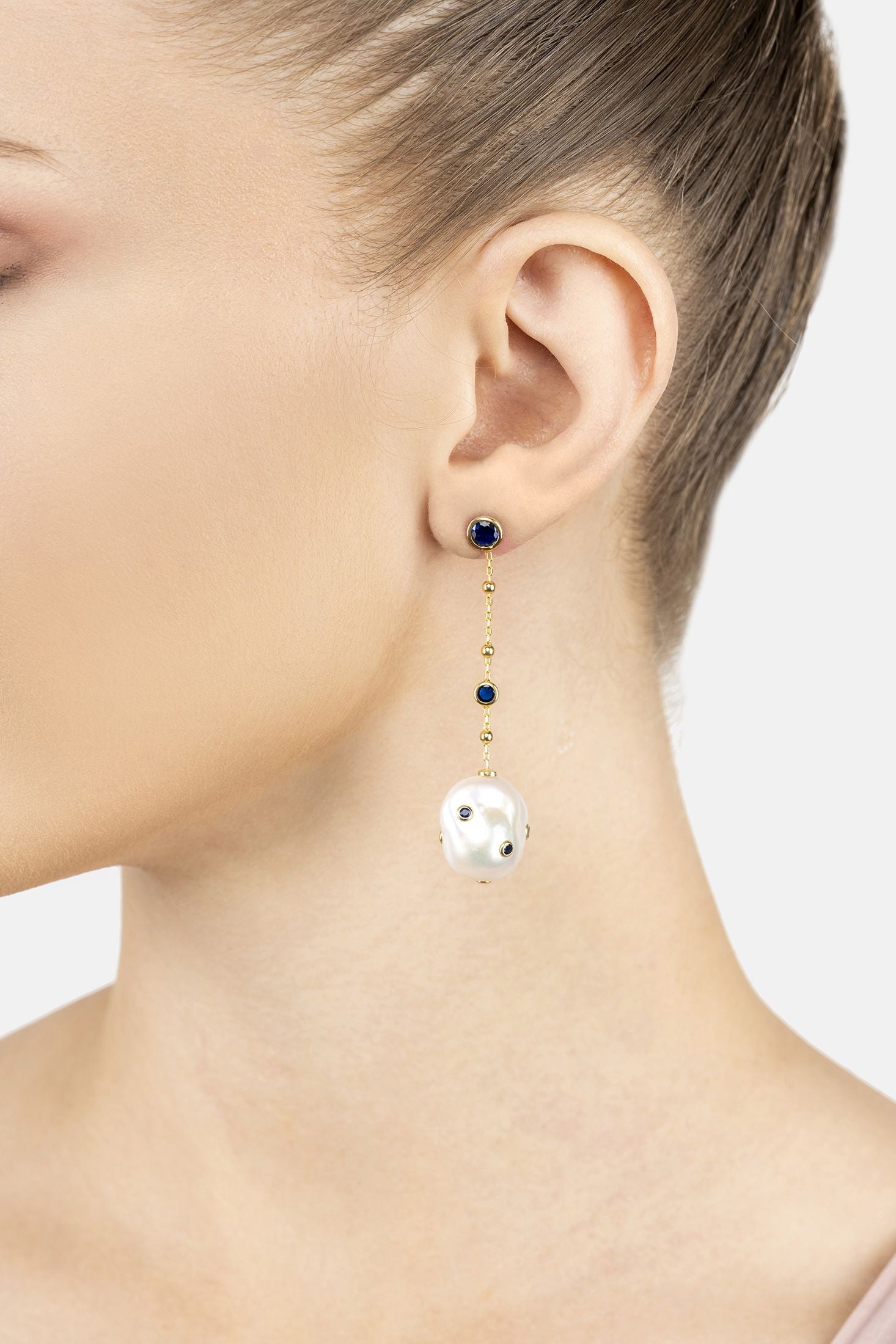 Angled view of Polka Dot Baroque Pearl Chain Drop Earrings Gold Sapphire, showing baroque pearl and pearl detailing, gold finish and the jewellery profile.