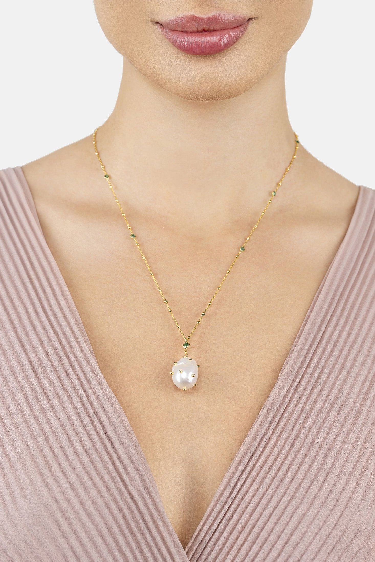 Gold necklace with a pearl pendant worn by a model against a neutral background
