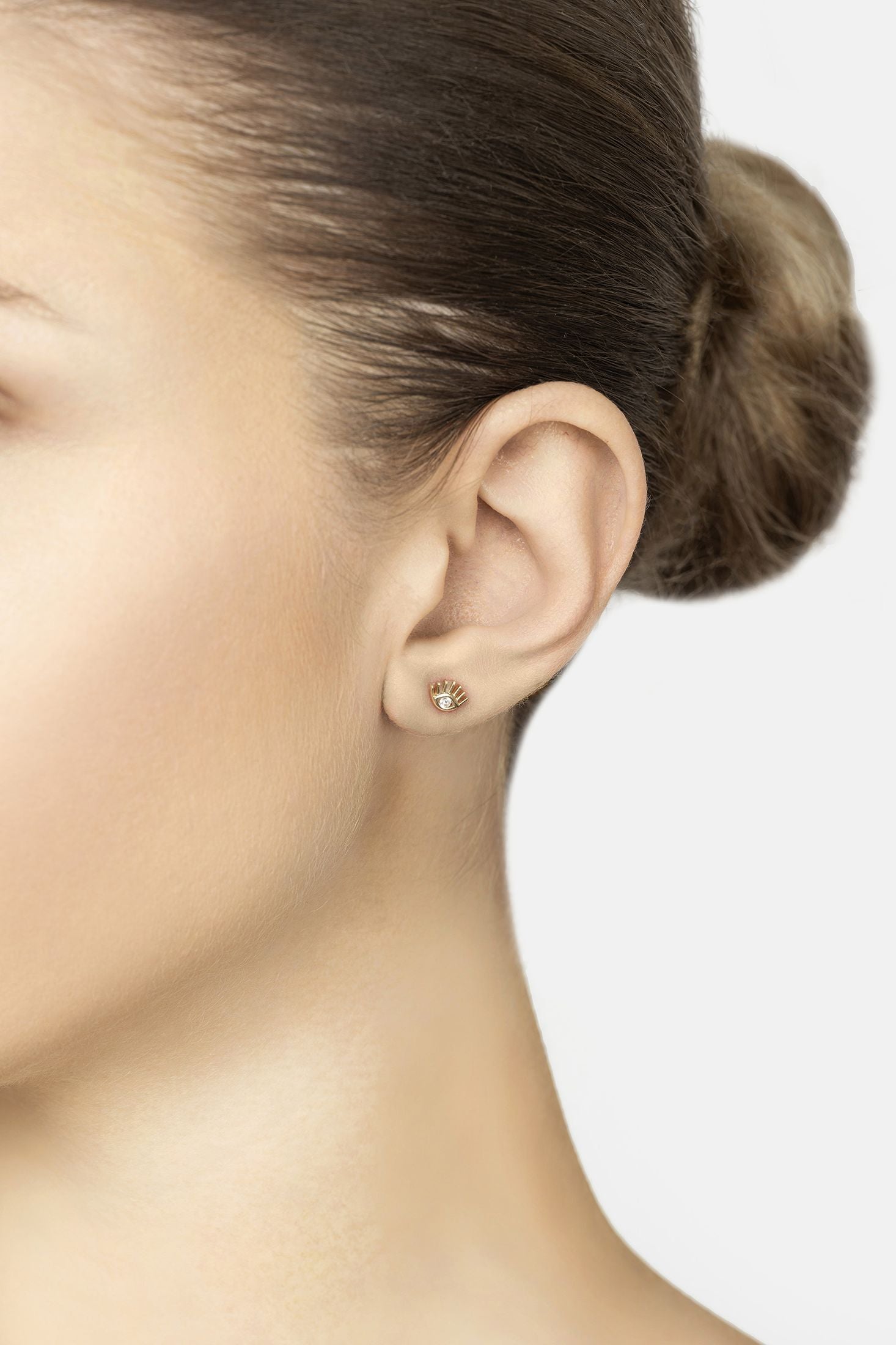 Close-up of a person wearing a gold earring on a plain background