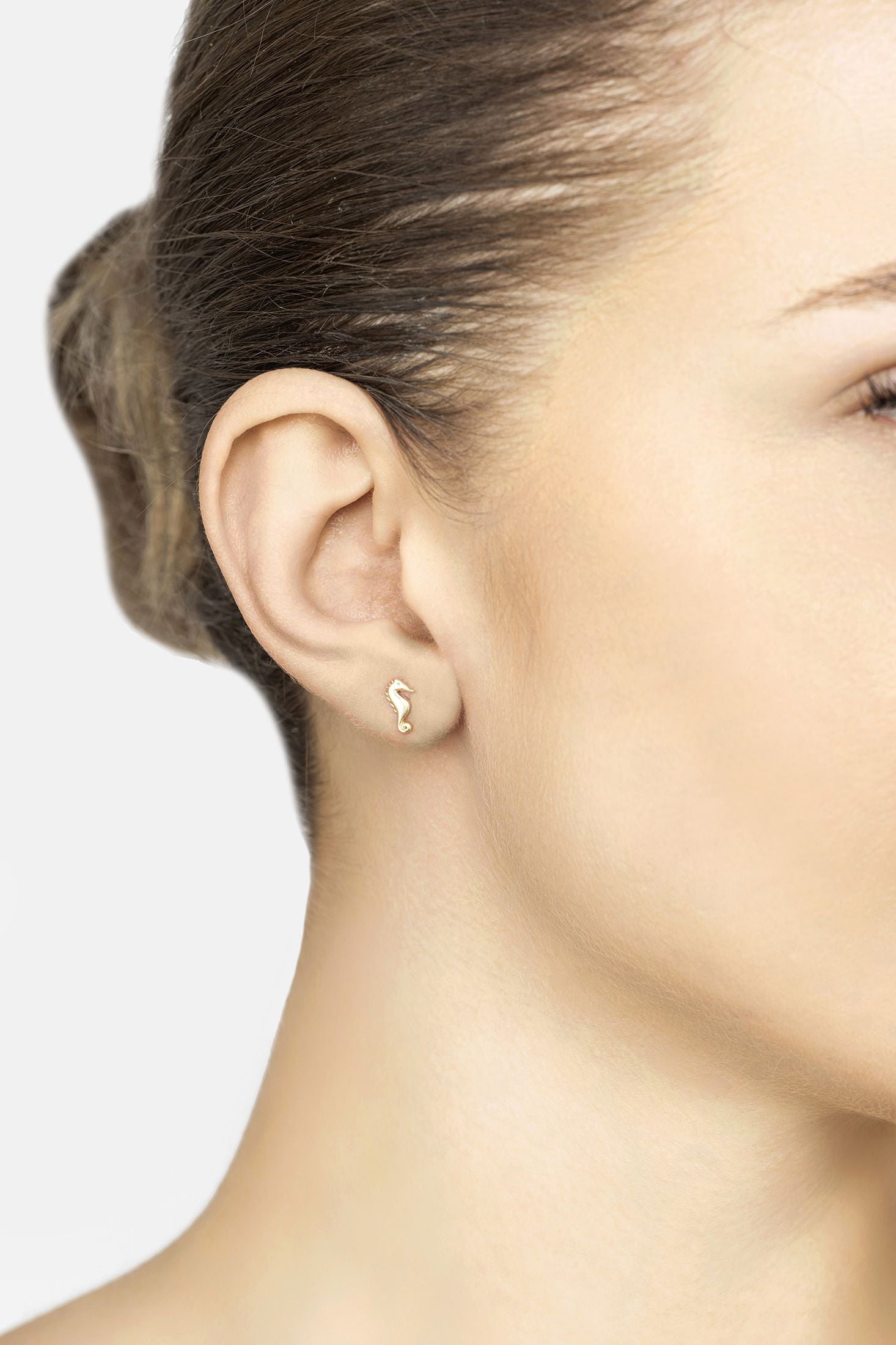 Close-up of a person wearing a gold earring with a seahorse design on a plain background