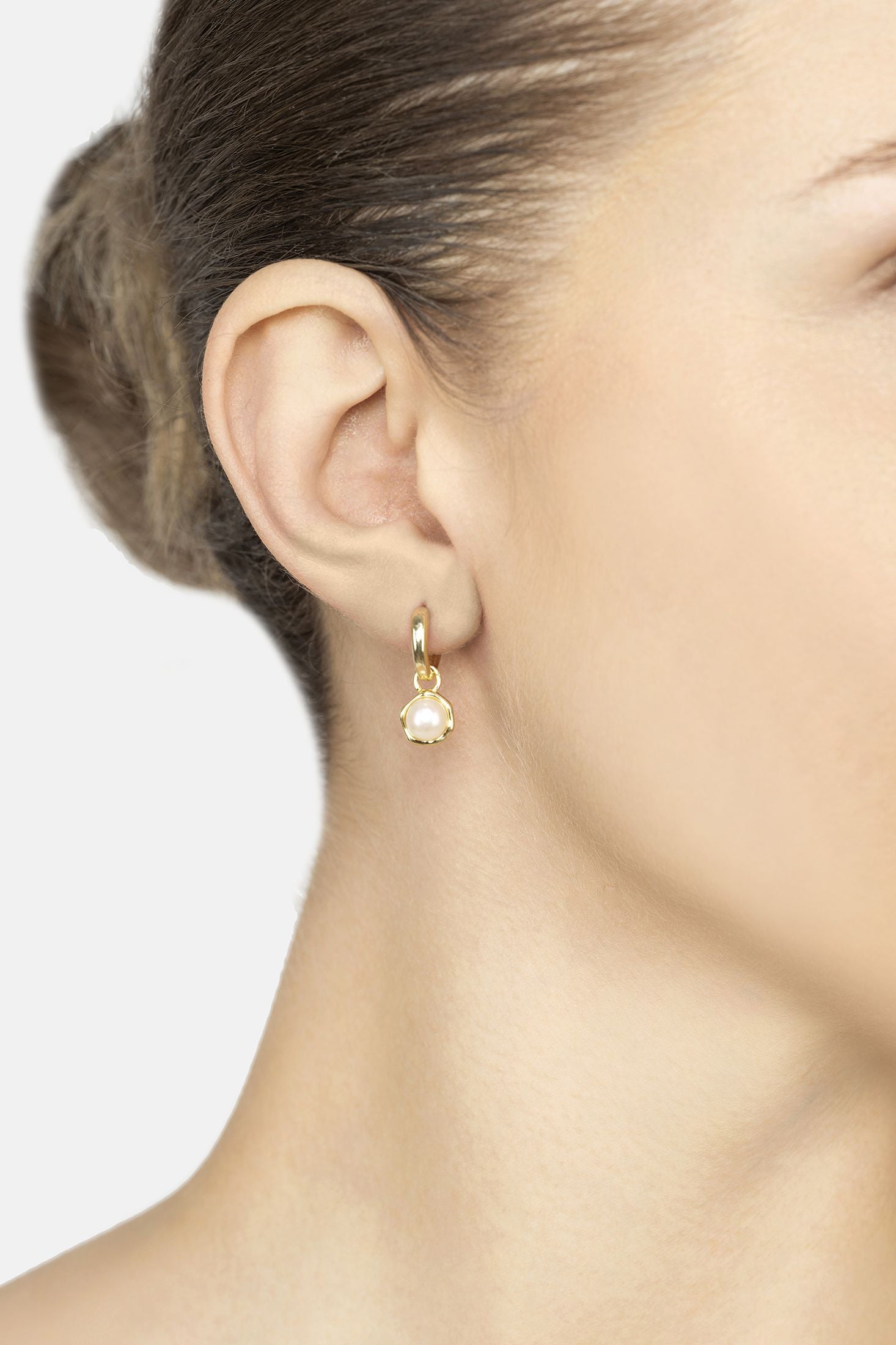 Close-up of a person wearing a gold earring with a pearl drop on a neutral background