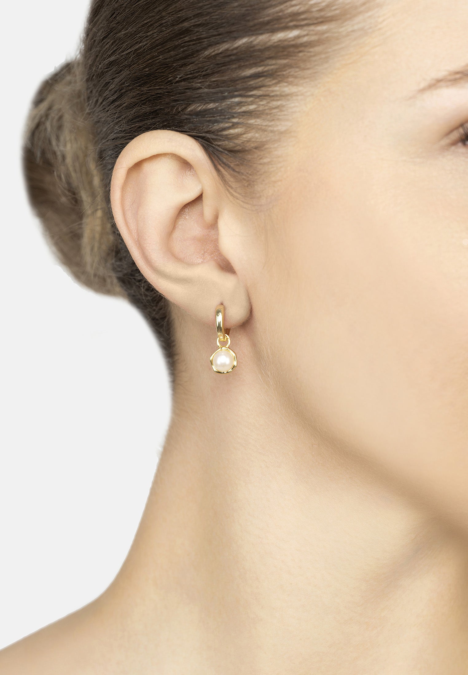 Close-up of a person wearing a gold earring with a pearl drop on a neutral background