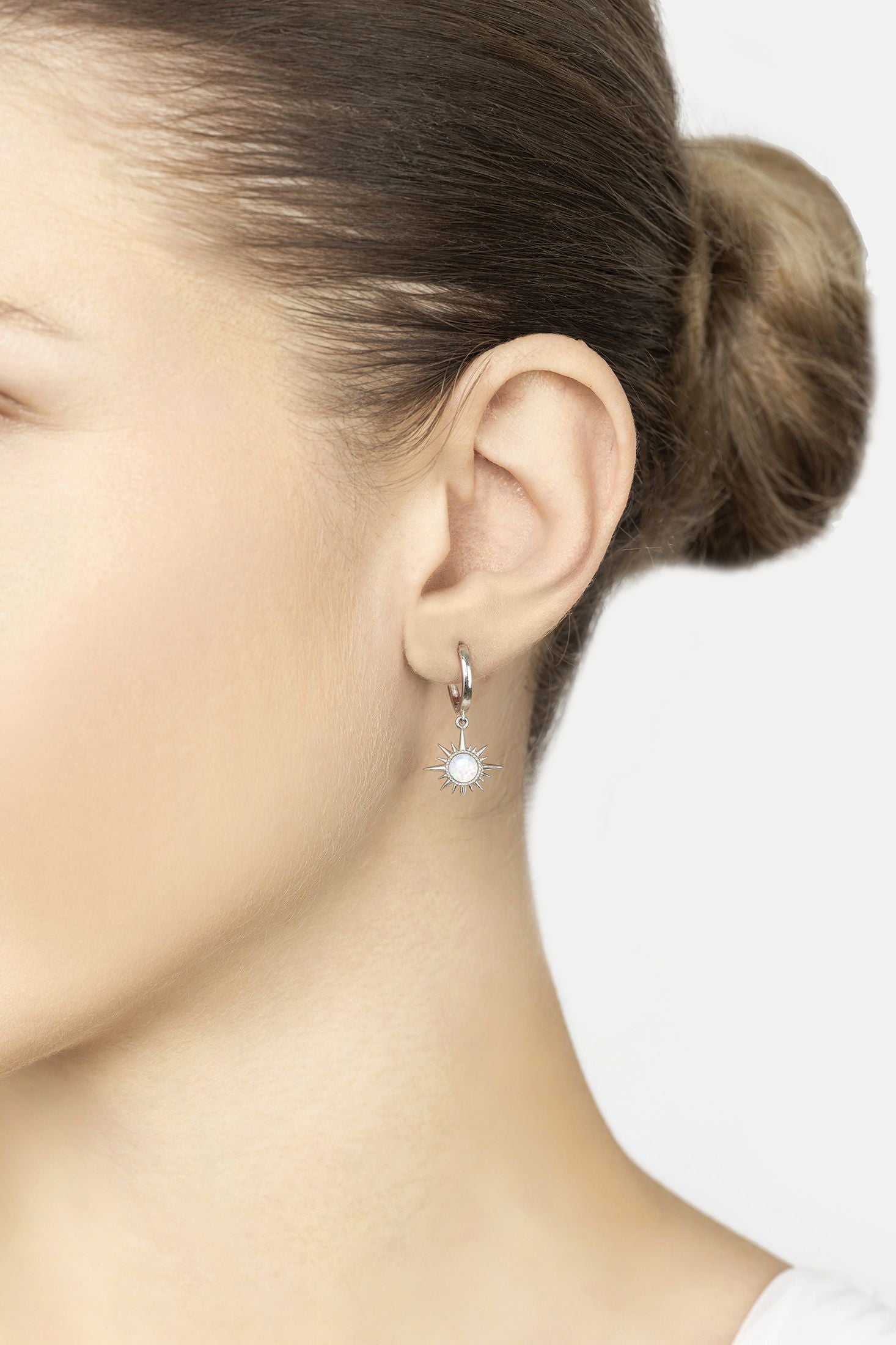 Close-up of a person wearing a silver earring with a clear gemstone on a white background