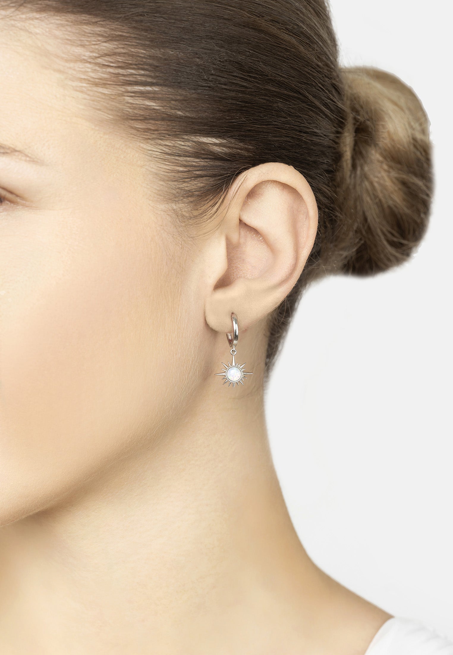 Close-up of a person wearing a silver earring with a clear gemstone on a white background