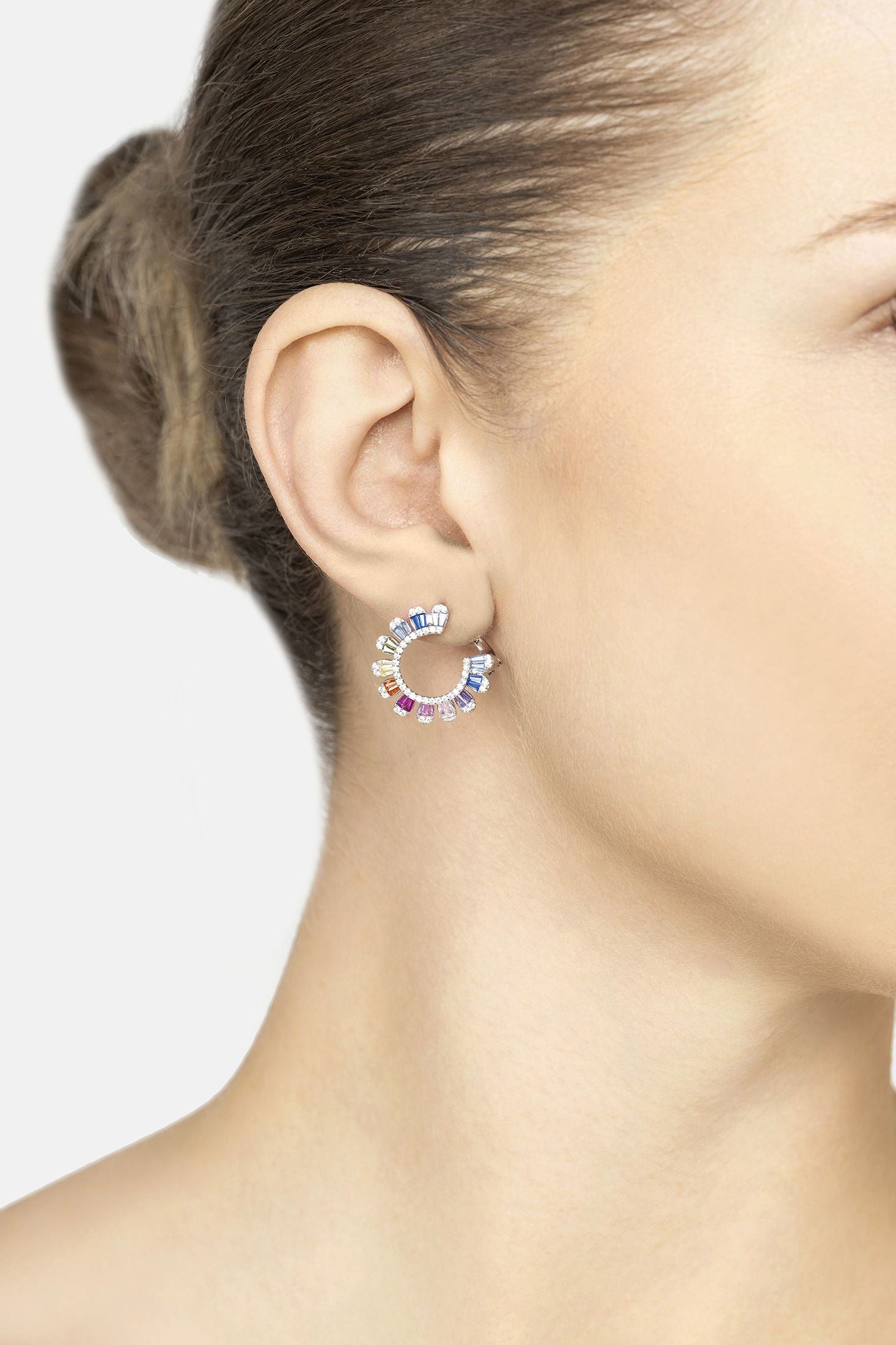 Close-up of a woman wearing colorful hoop earrings with a neutral background