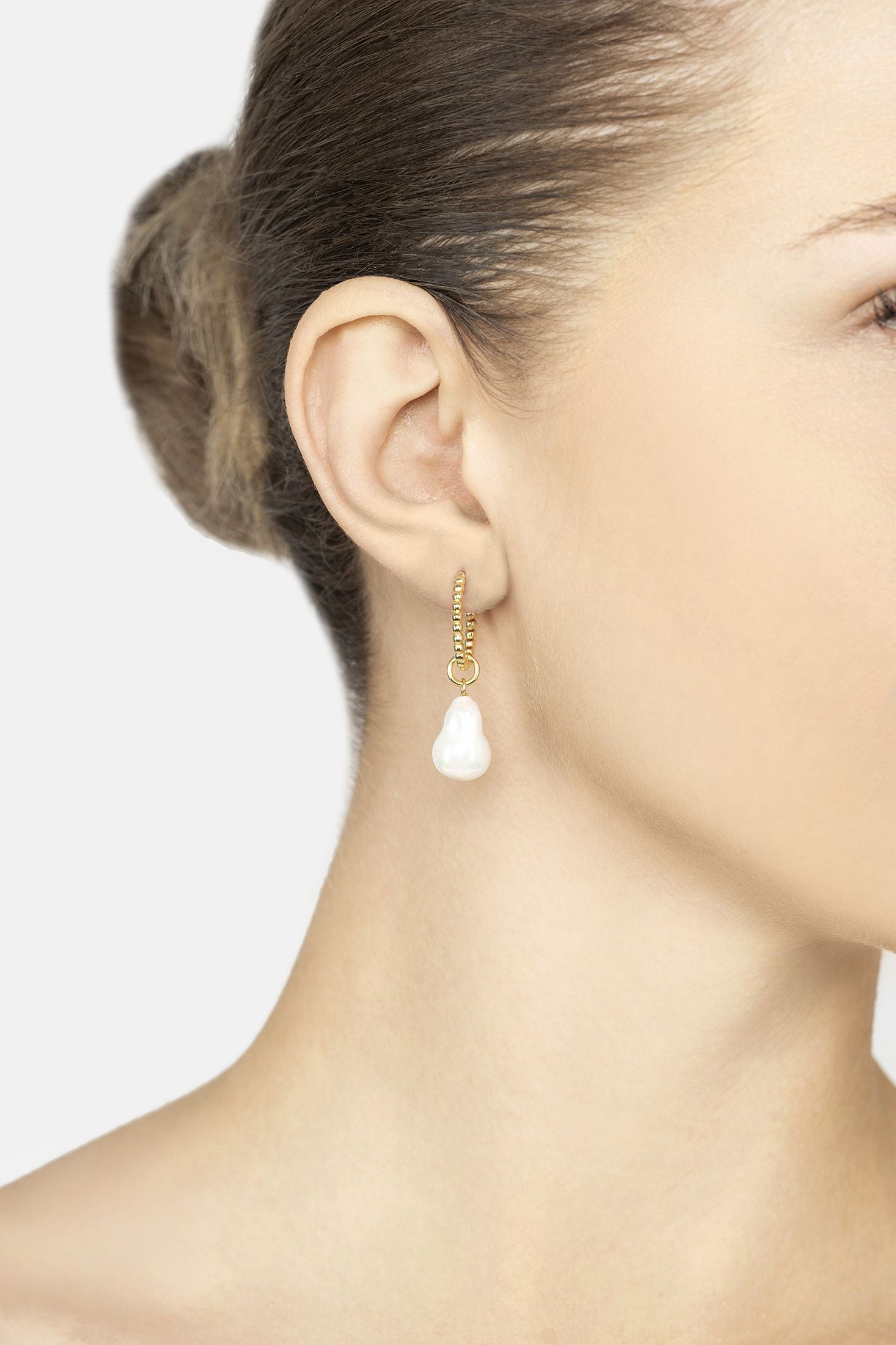 Close-up of a woman wearing a gold earring with a pearl on the bottom on a plain background