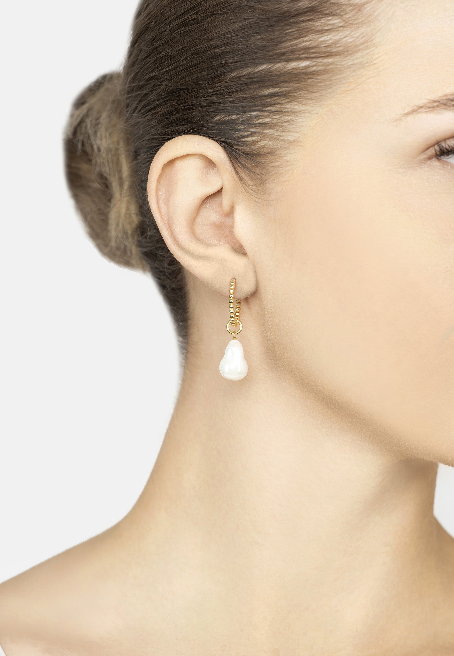 Close-up of a woman wearing a gold earring with a pearl on the bottom on a plain background