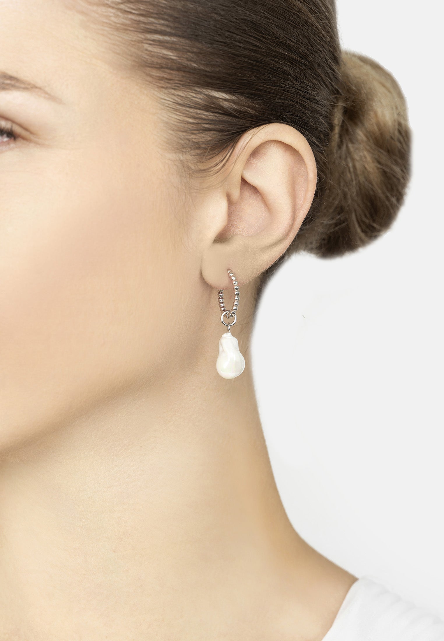 Pearl earring worn by a person on a plain background