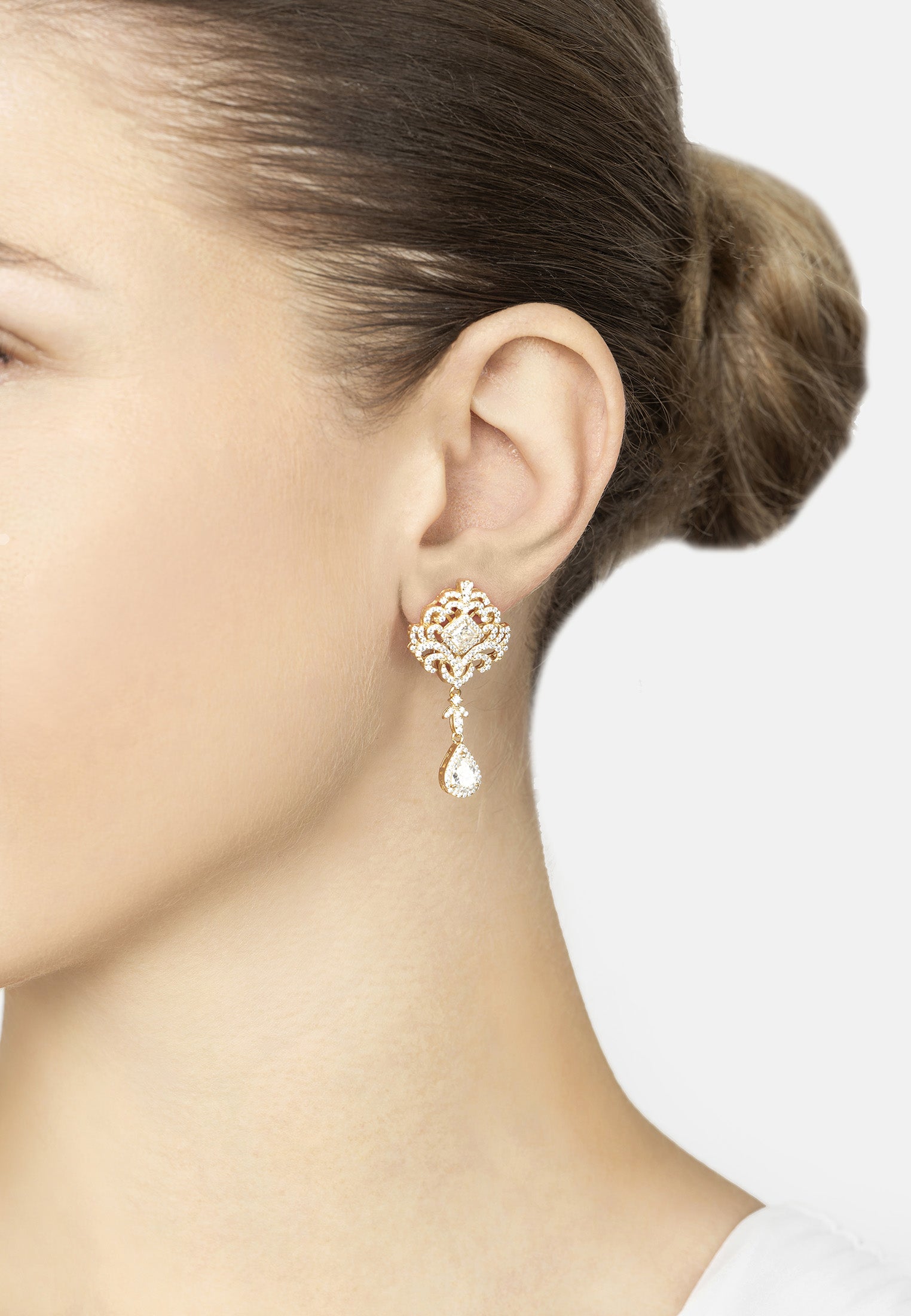 Close-up of a person wearing a gold earring with a clear gemstone on a plain background
