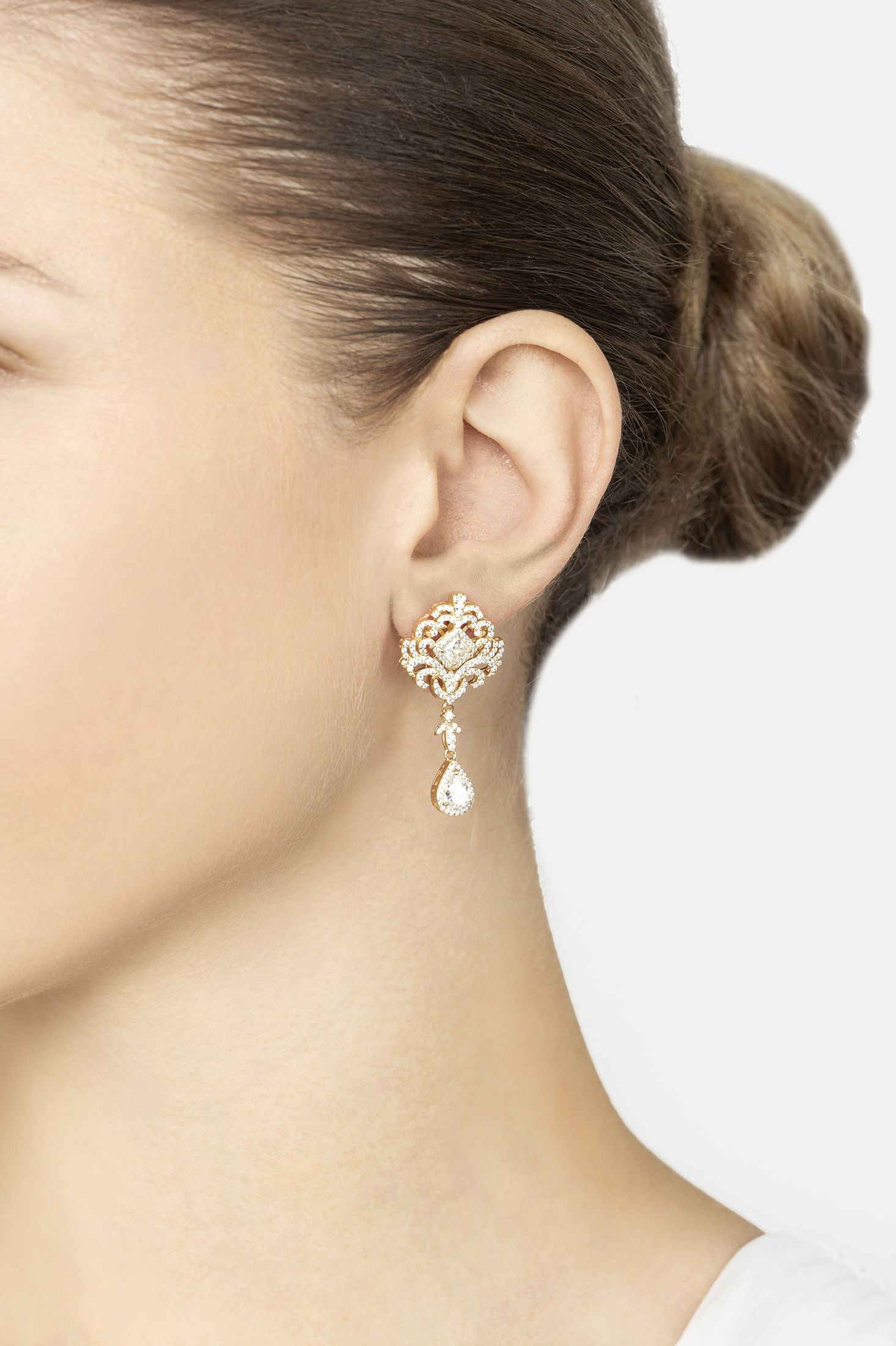 Close-up of a person wearing a gold earring with a clear gemstone on a plain background