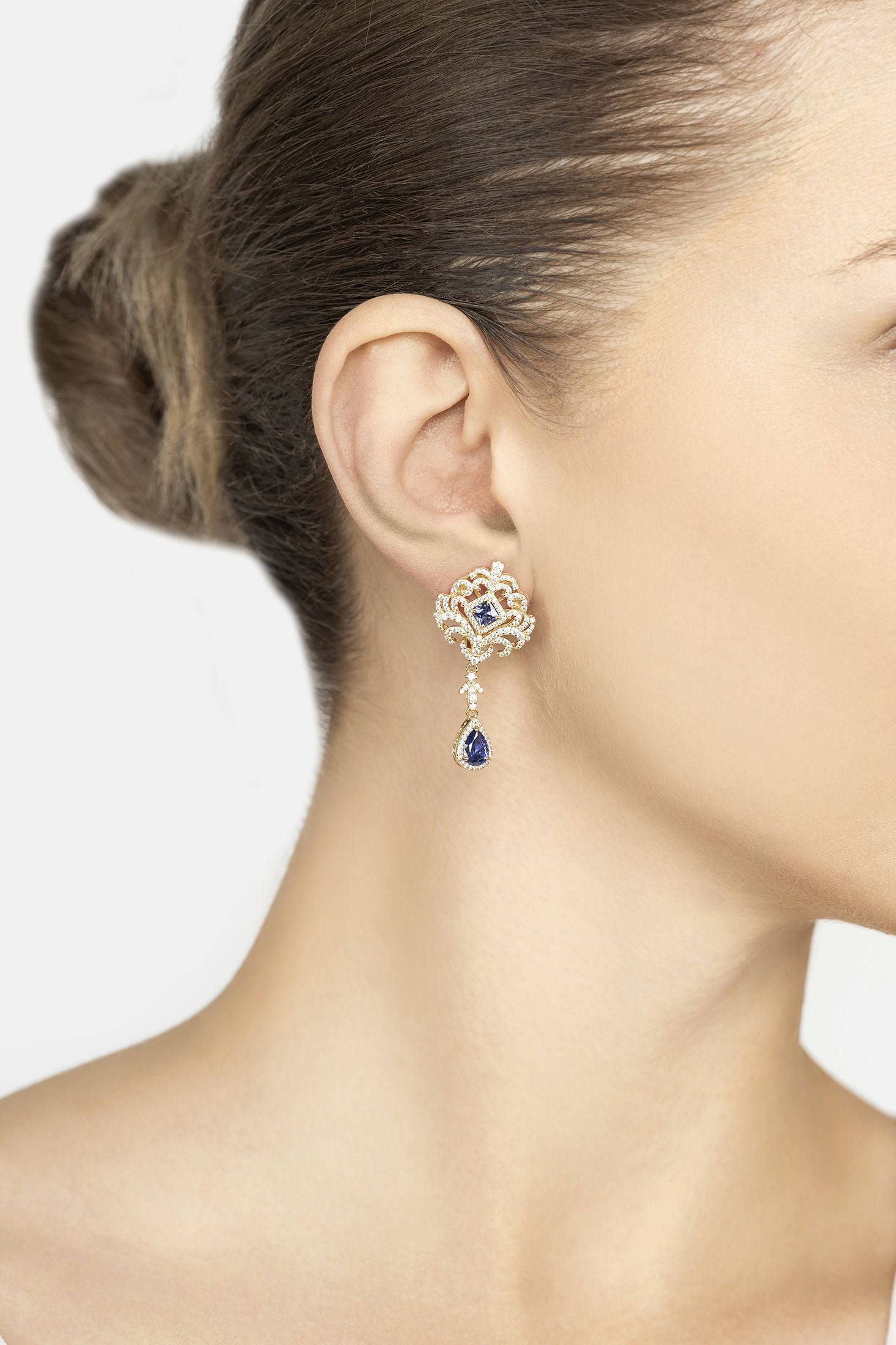 Close-up of a woman wearing a decorative gold earring with a blue gemstone on a plain background