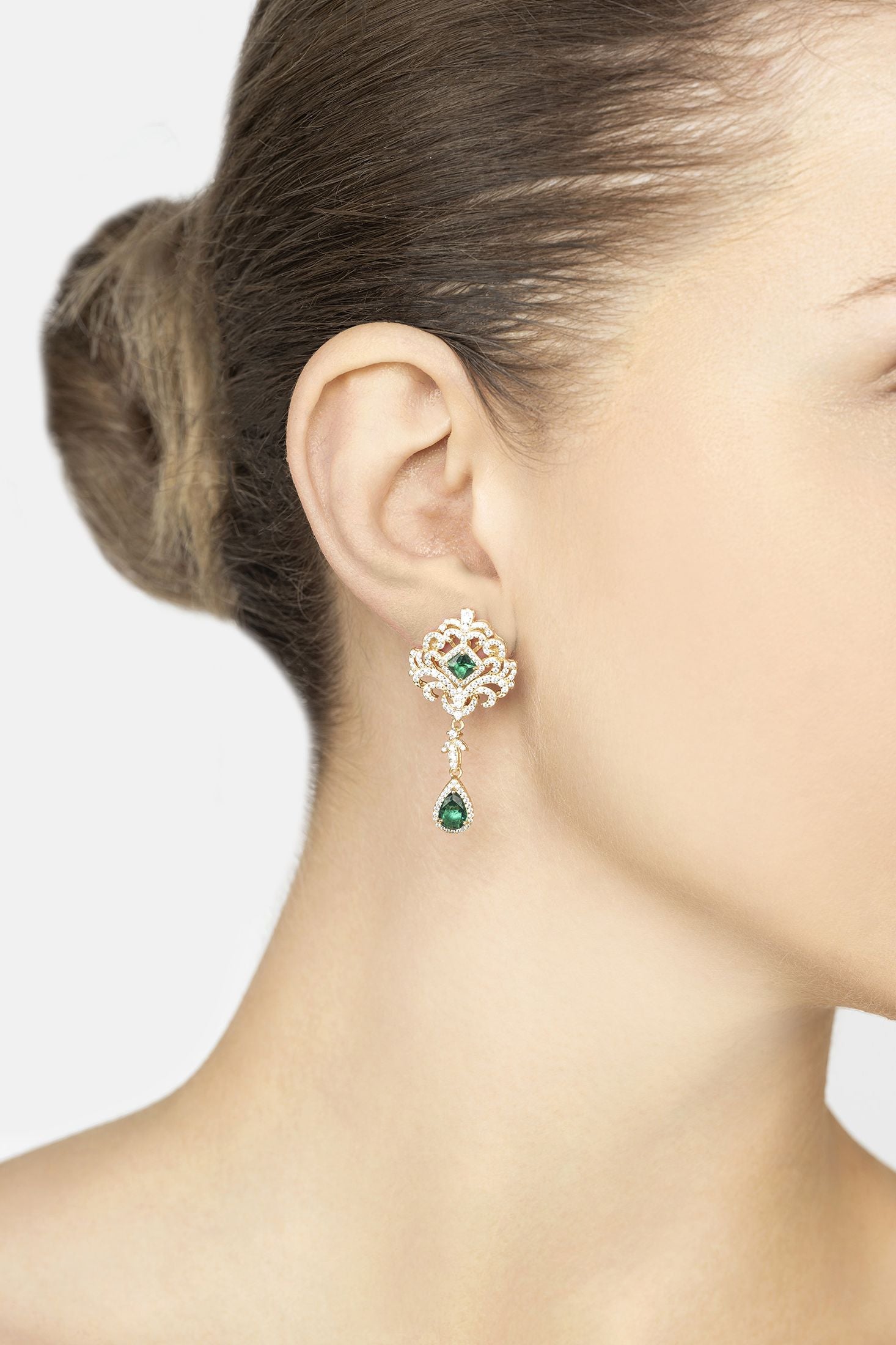 Close-up of a woman wearing a gold earring with green gemstones on a plain background