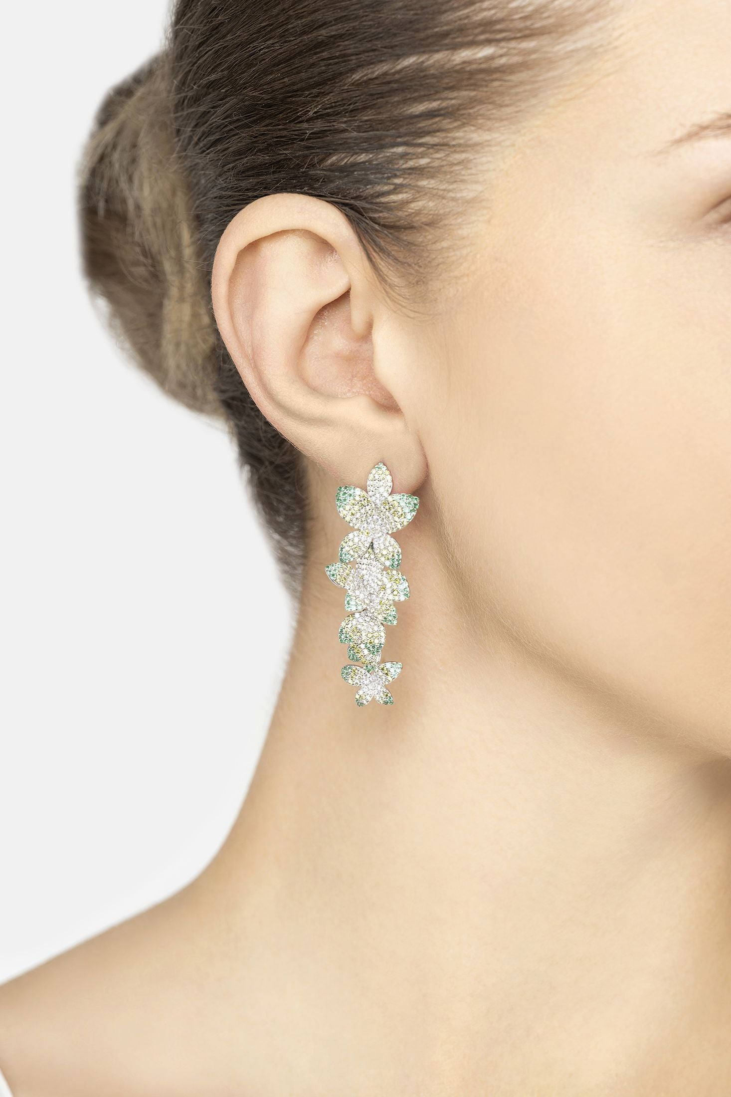 Close-up of a woman wearing a floral earring with green gemstones on a white background
