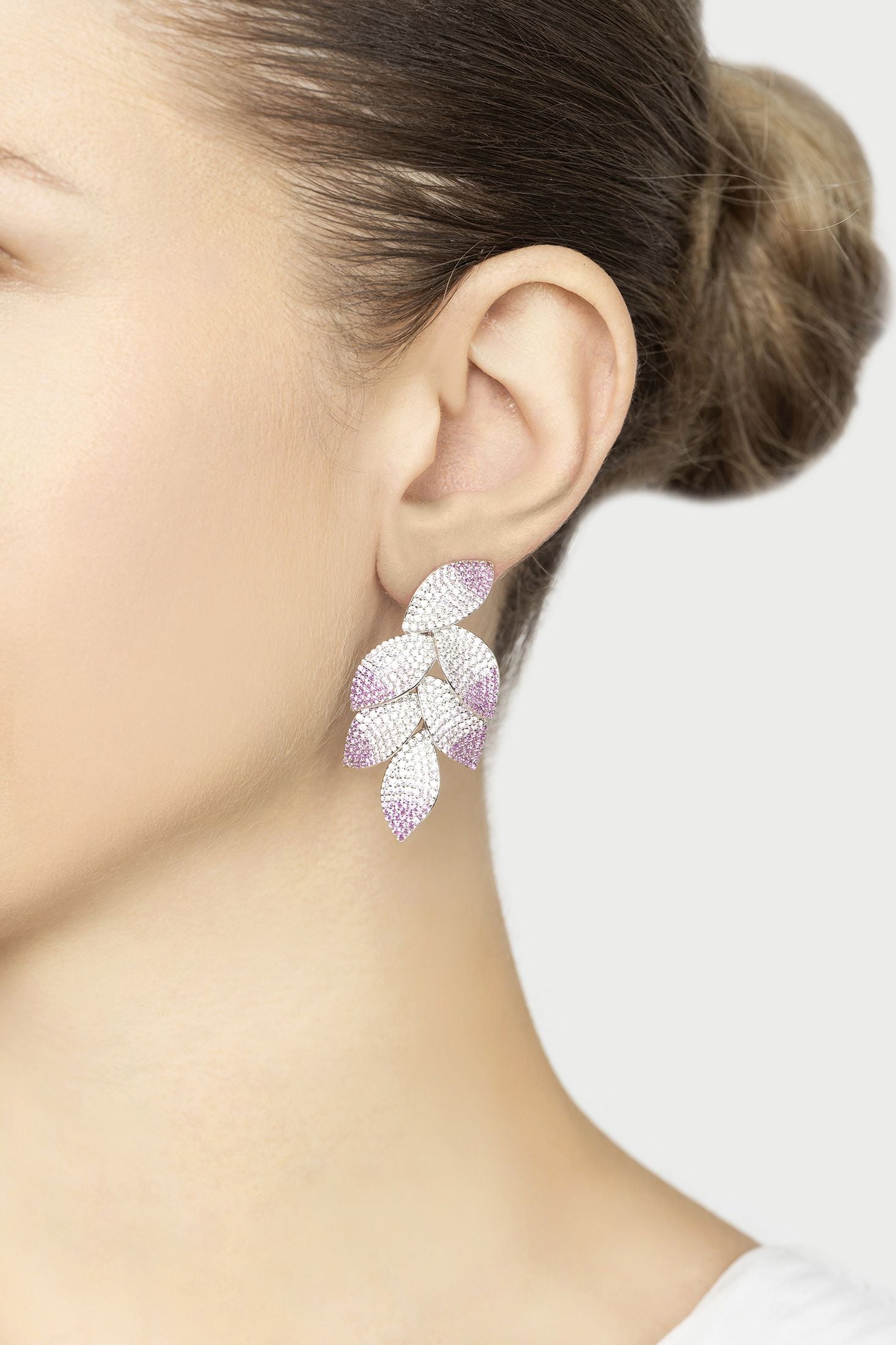 Close-up of a person wearing pink leaf-shaped earrings on a white background