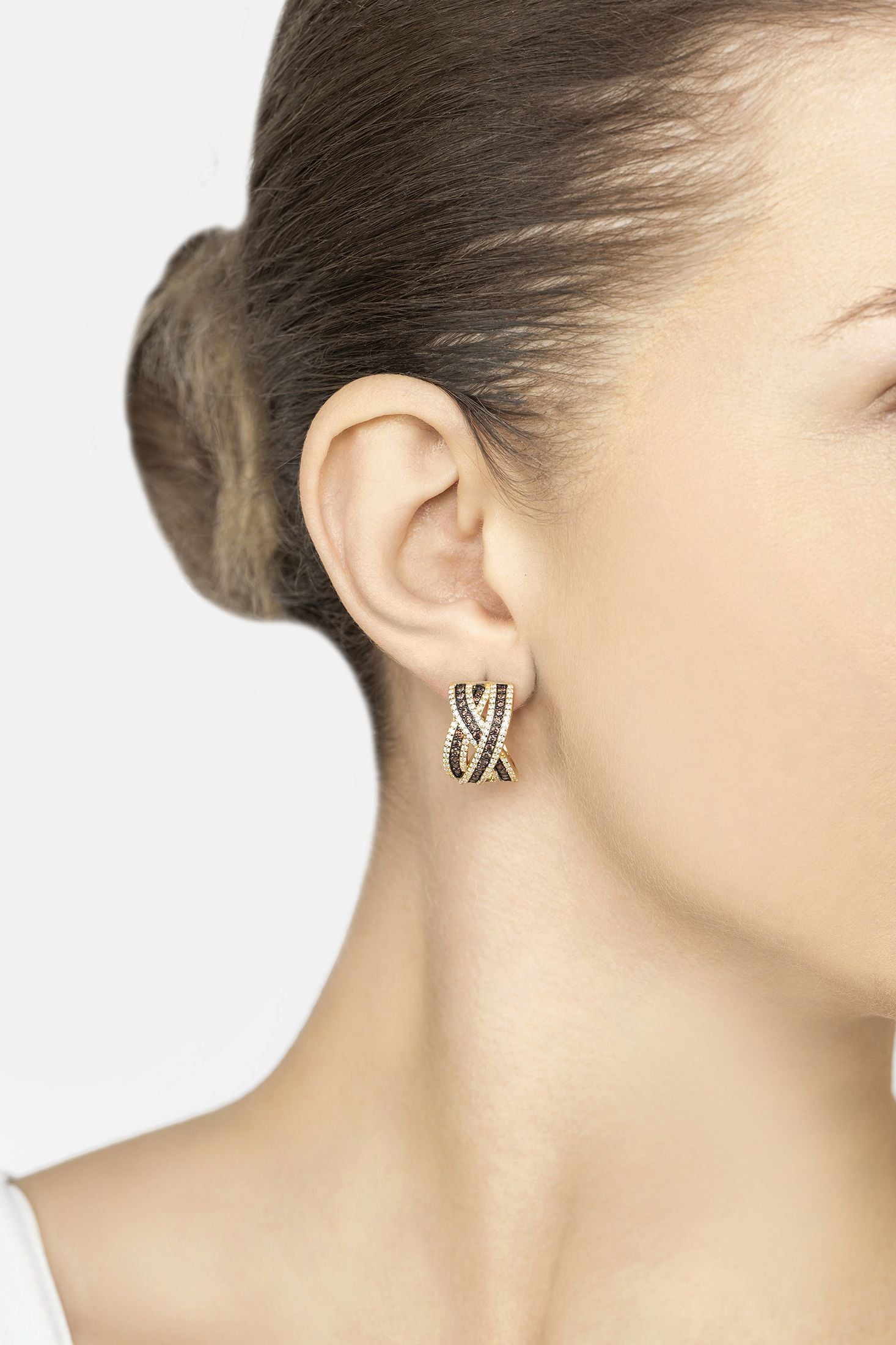 Close-up of a woman wearing a gold and black crossover earring with a plain background