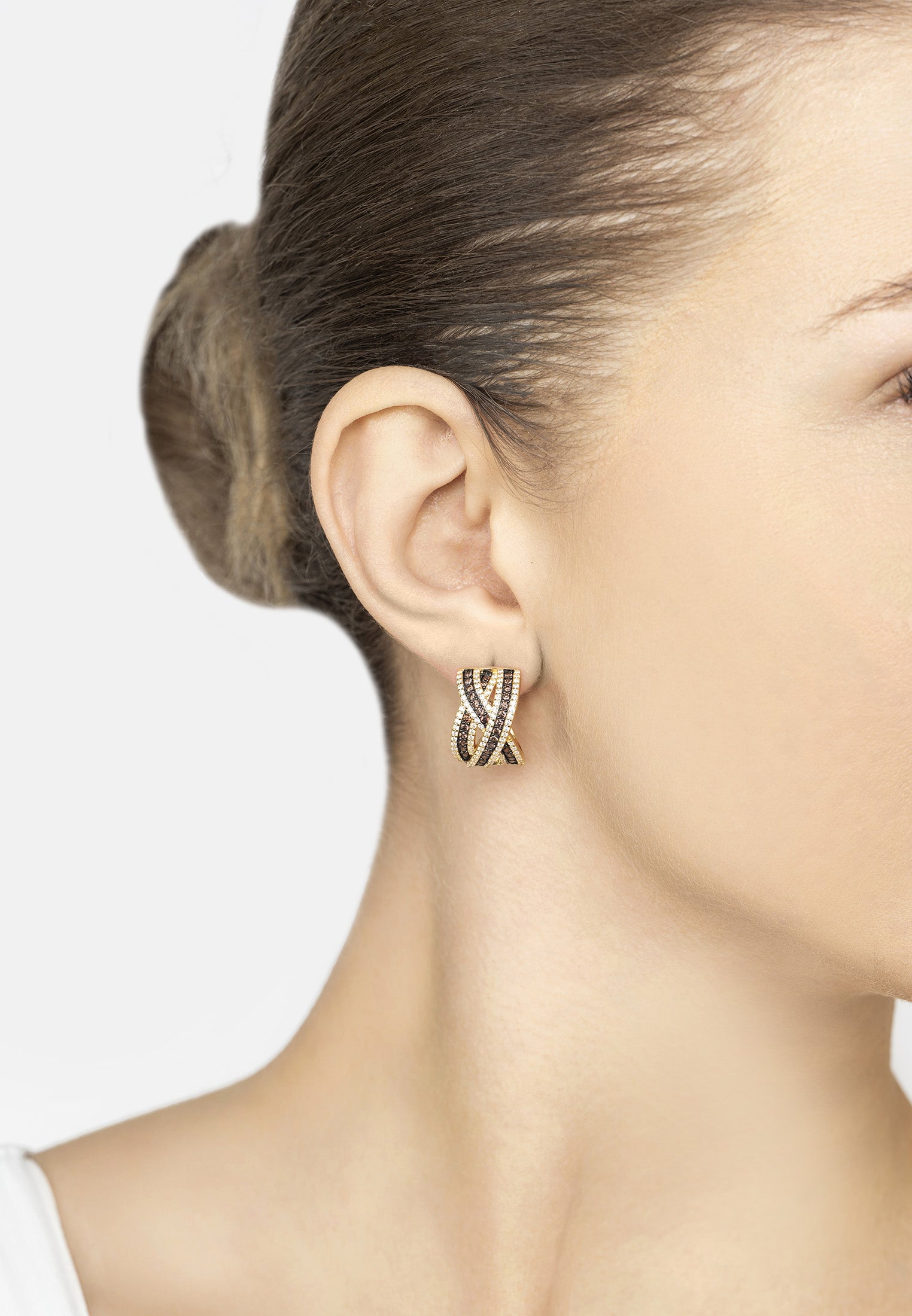Close-up of a woman wearing a gold and black crossover earring with a plain background