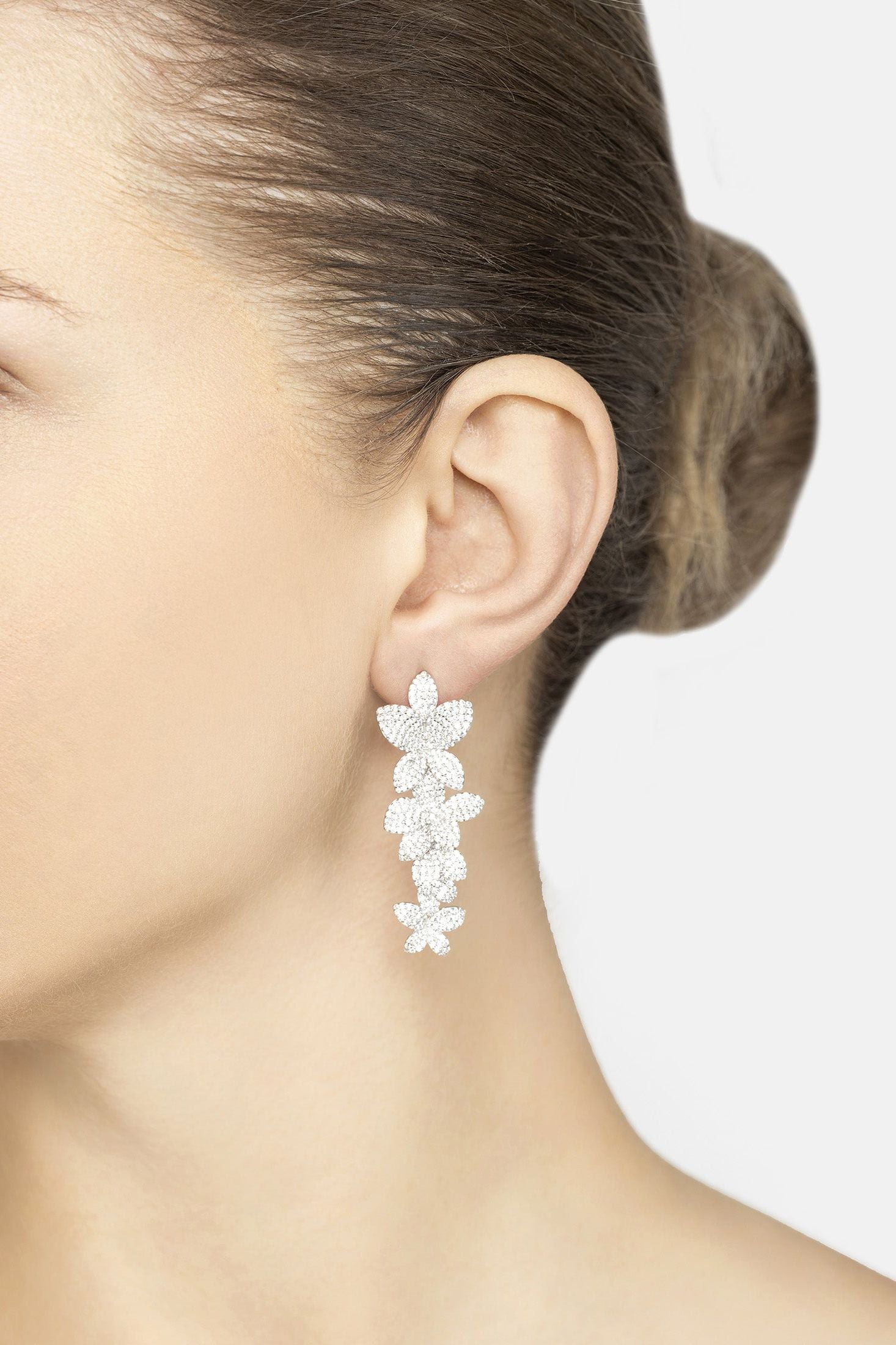Close-up of a person wearing a floral silver earring on a plain background