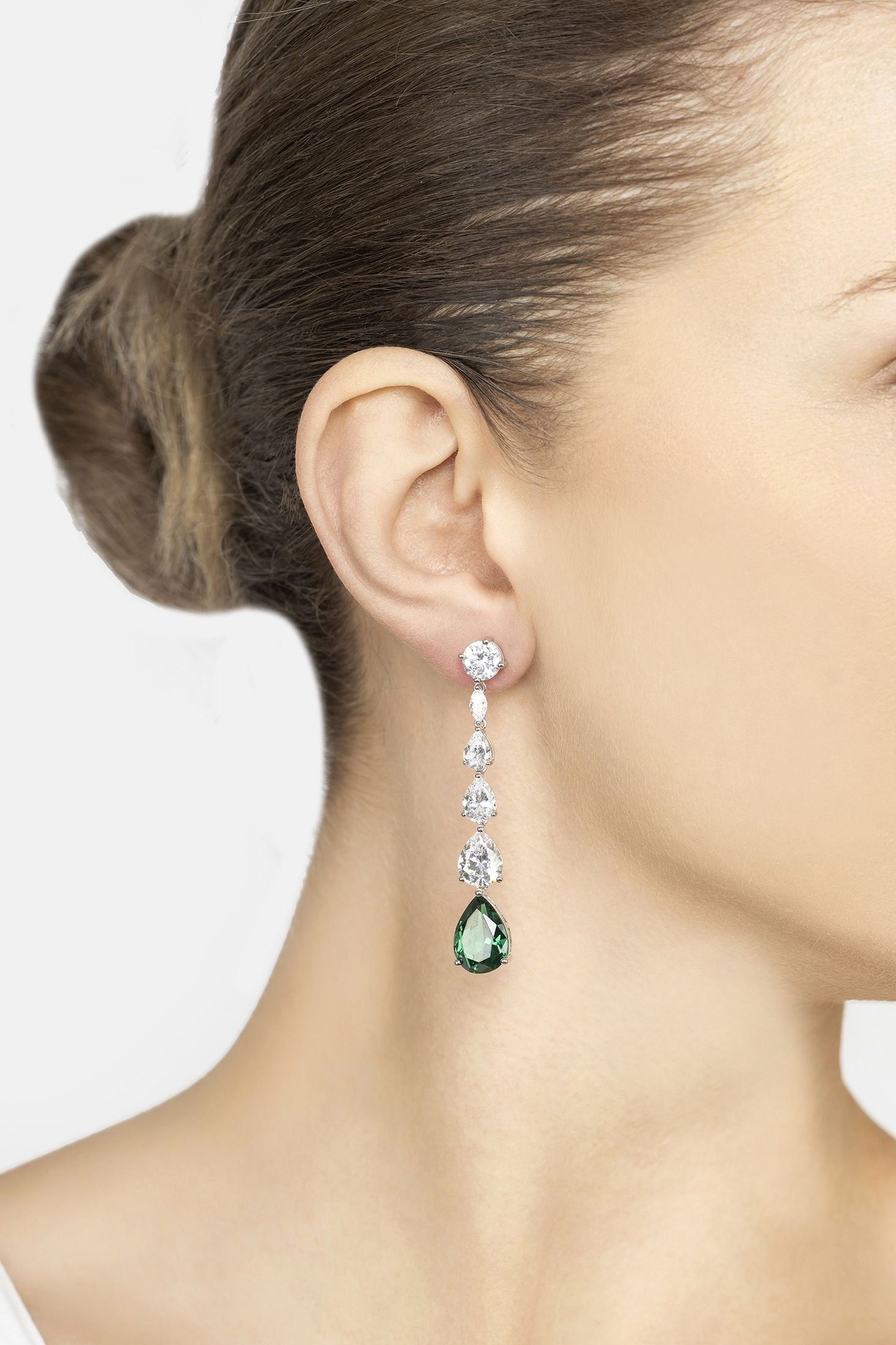 Close-up of a woman wearing a green teardrop earring with multiple diamonds on a white background
