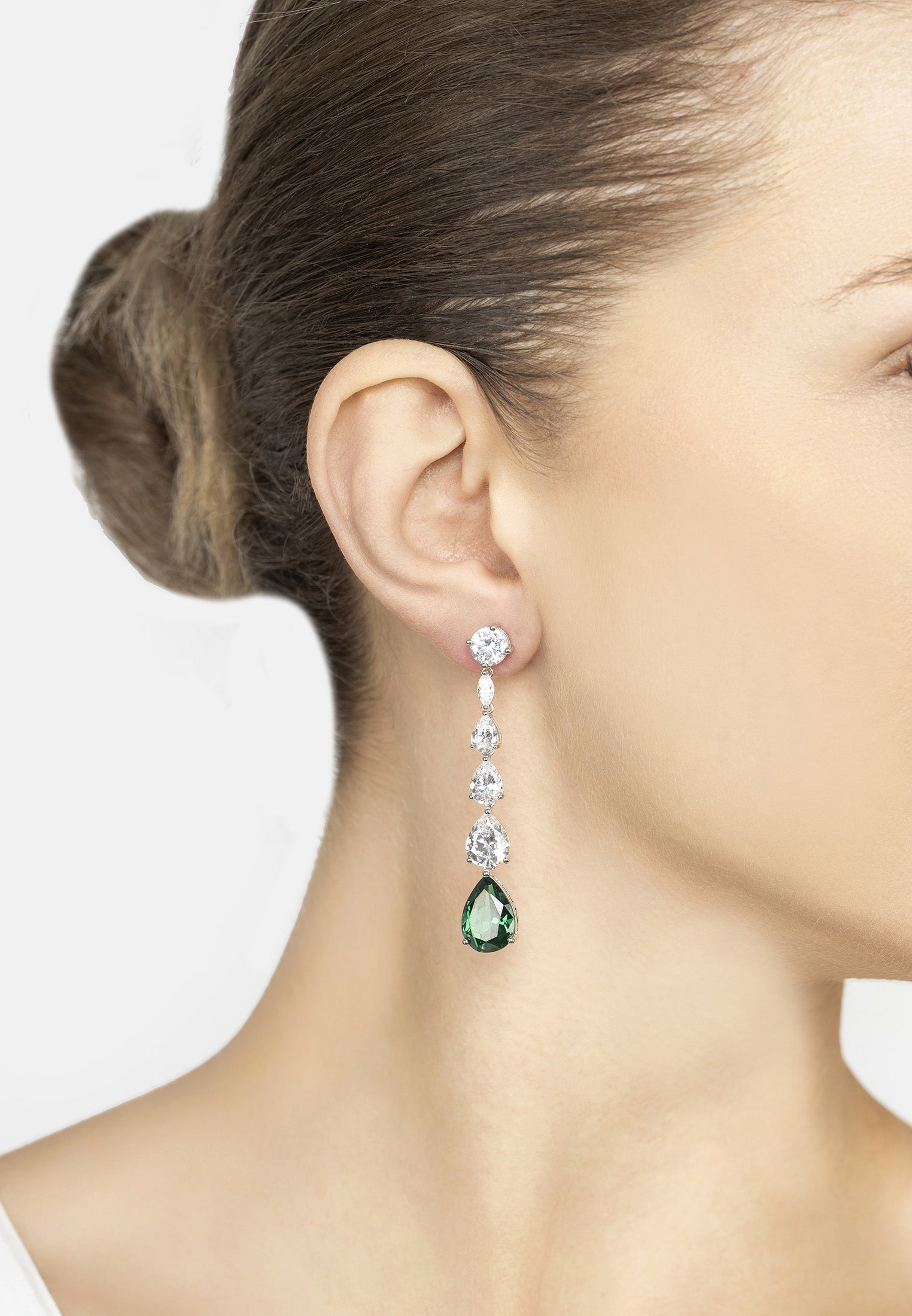 Close-up of a woman wearing a green teardrop earring with multiple diamonds on a white background
