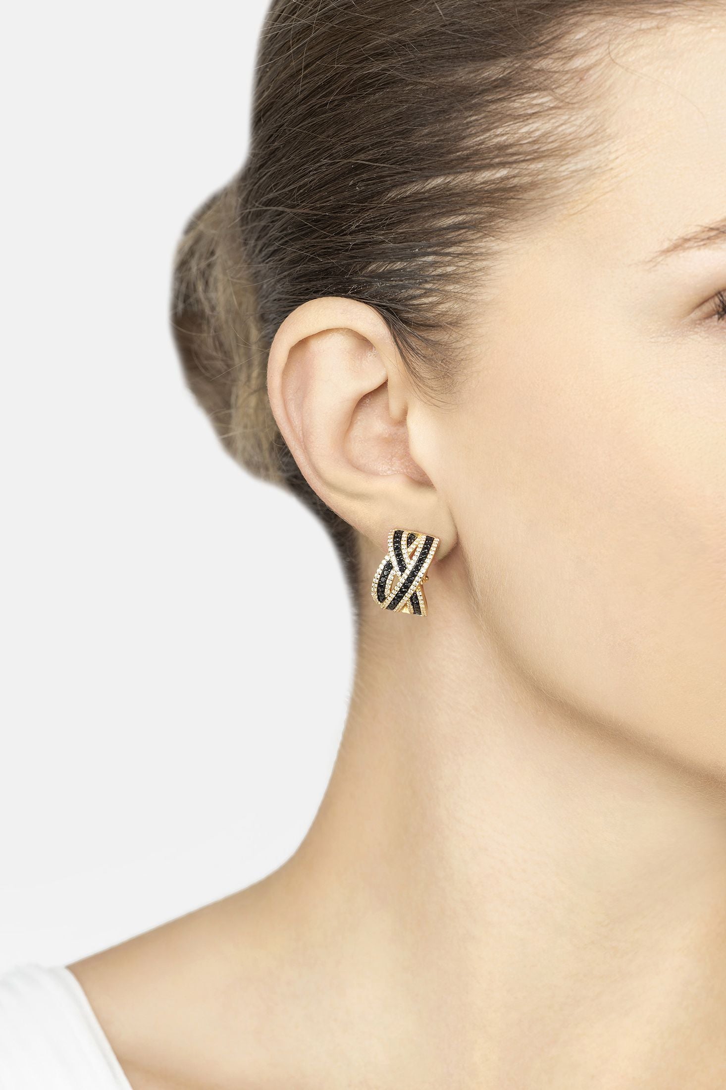 Close-up of a person wearing a gold and black earring on a plain background