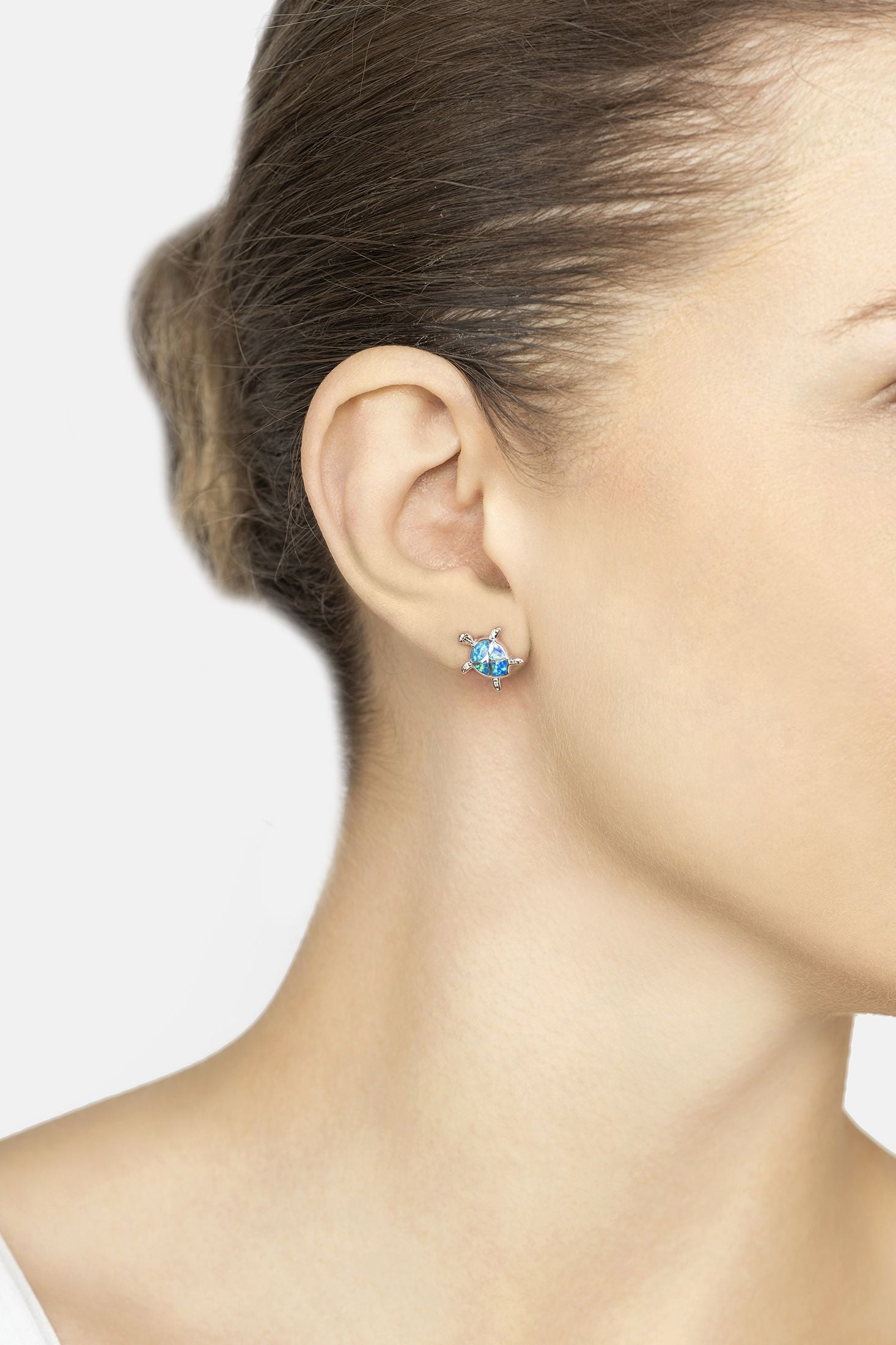 Close-up of a person wearing a blue gemstone earring on a plain background