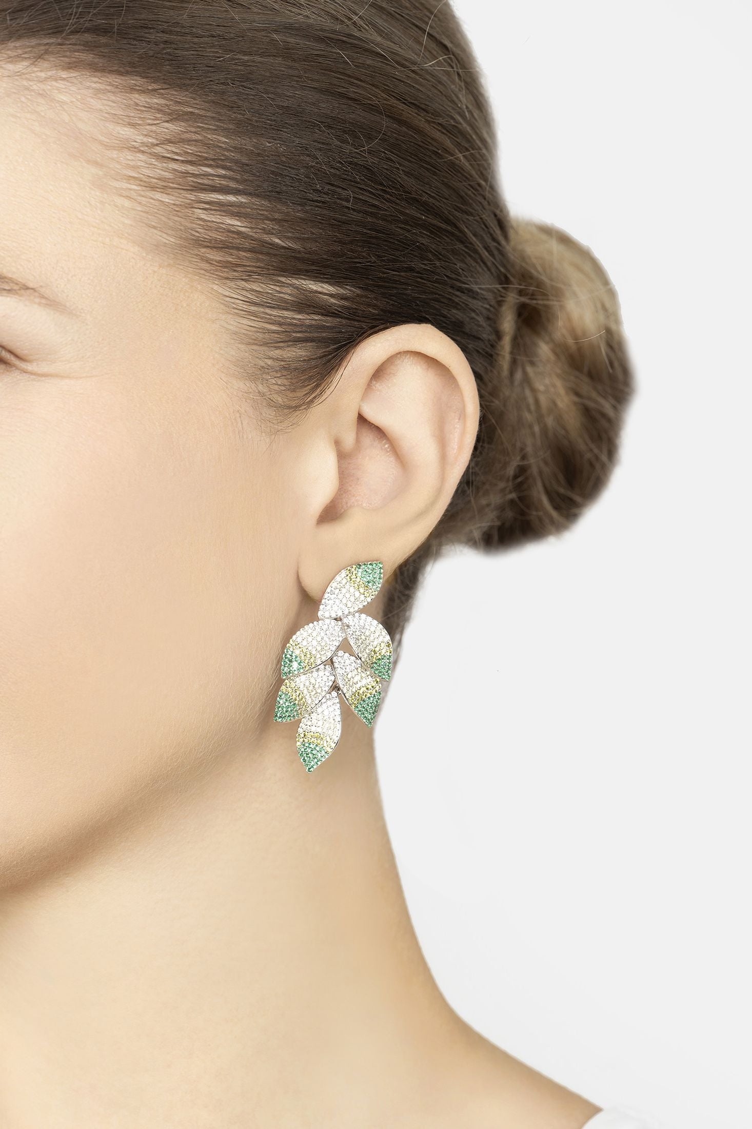 Close-up of a person wearing a leaf-shaped earring with green and white stones on a plain background