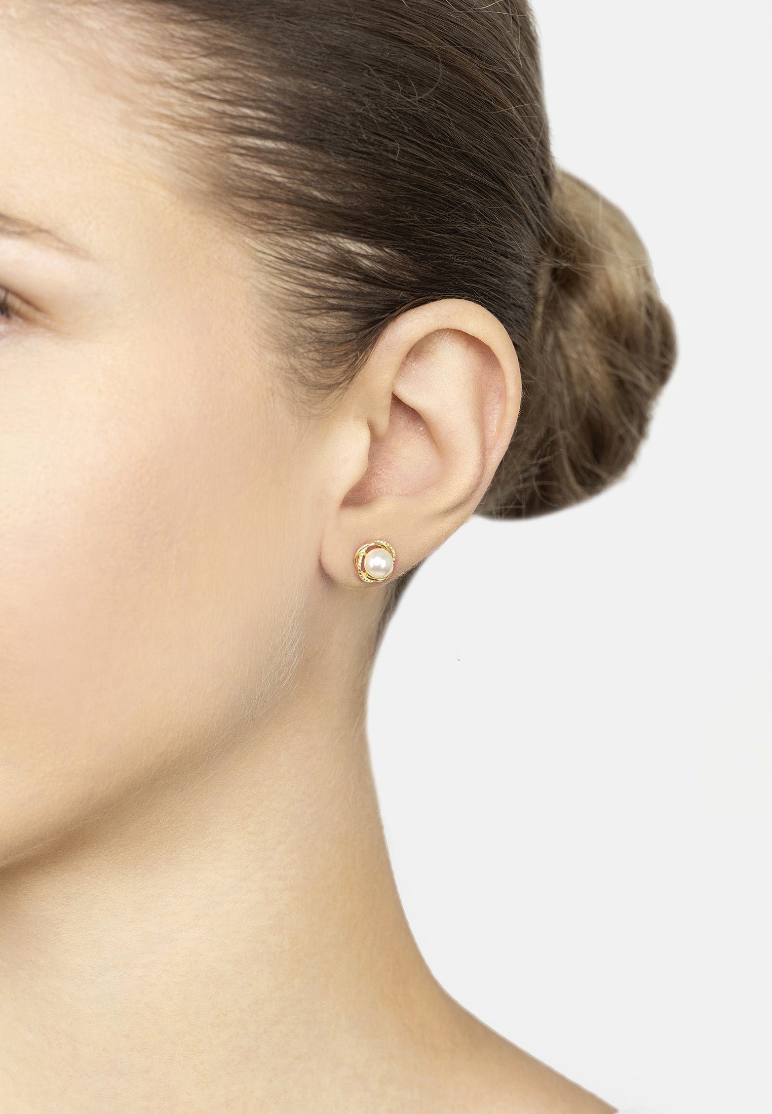 Close-up of a person wearing a gold earring on a plain background