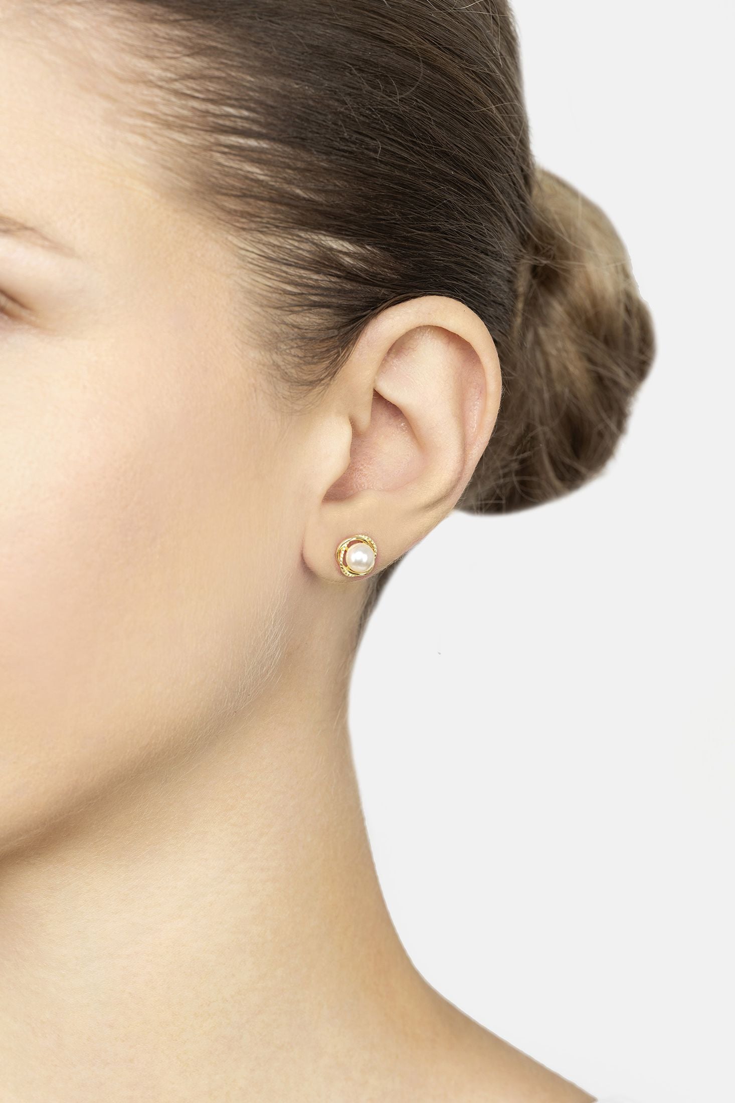 Close-up of a person wearing a gold earring on a plain background