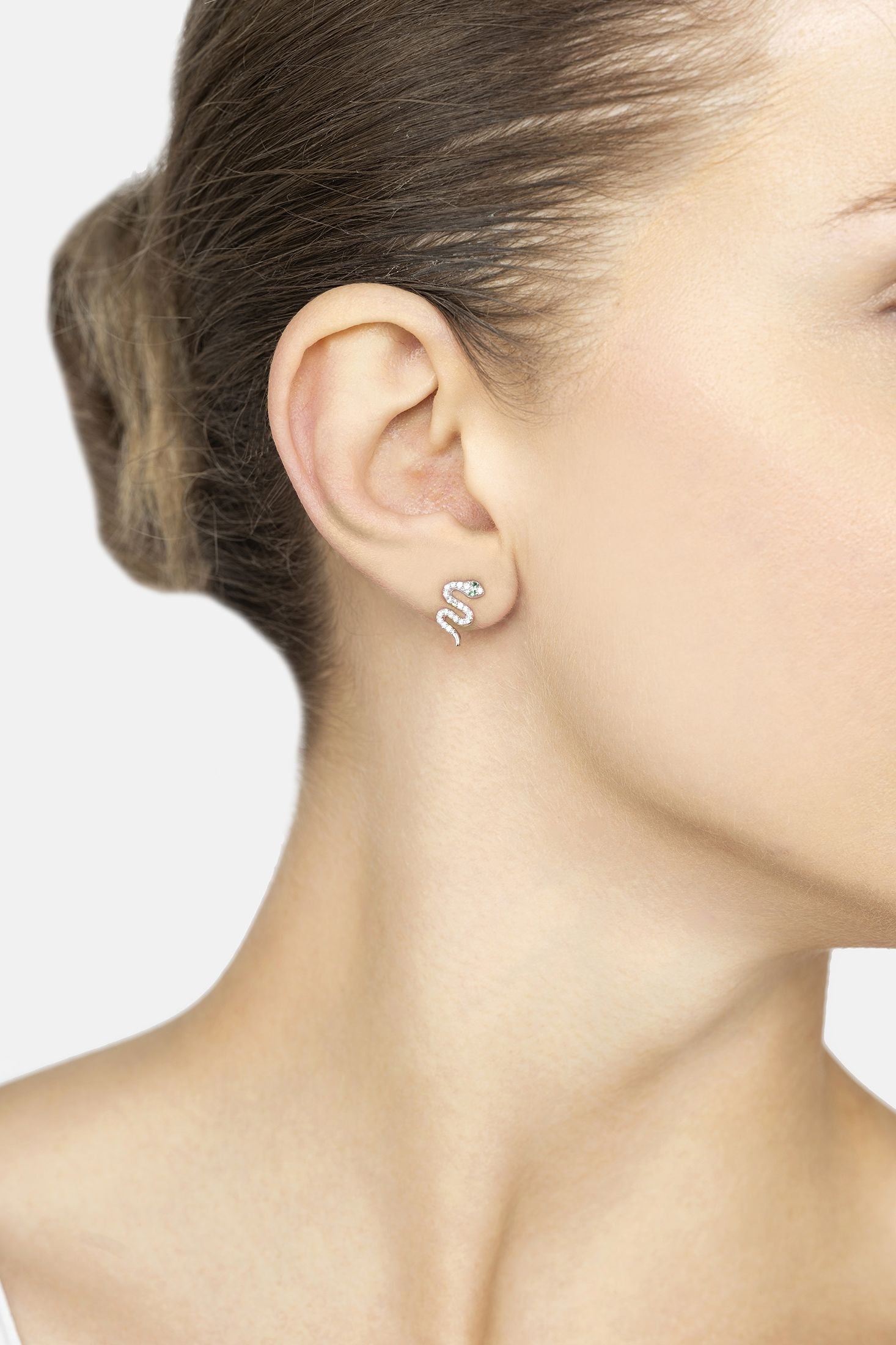 Close-up of a person wearing silver snake-shaped earrings on a plain background