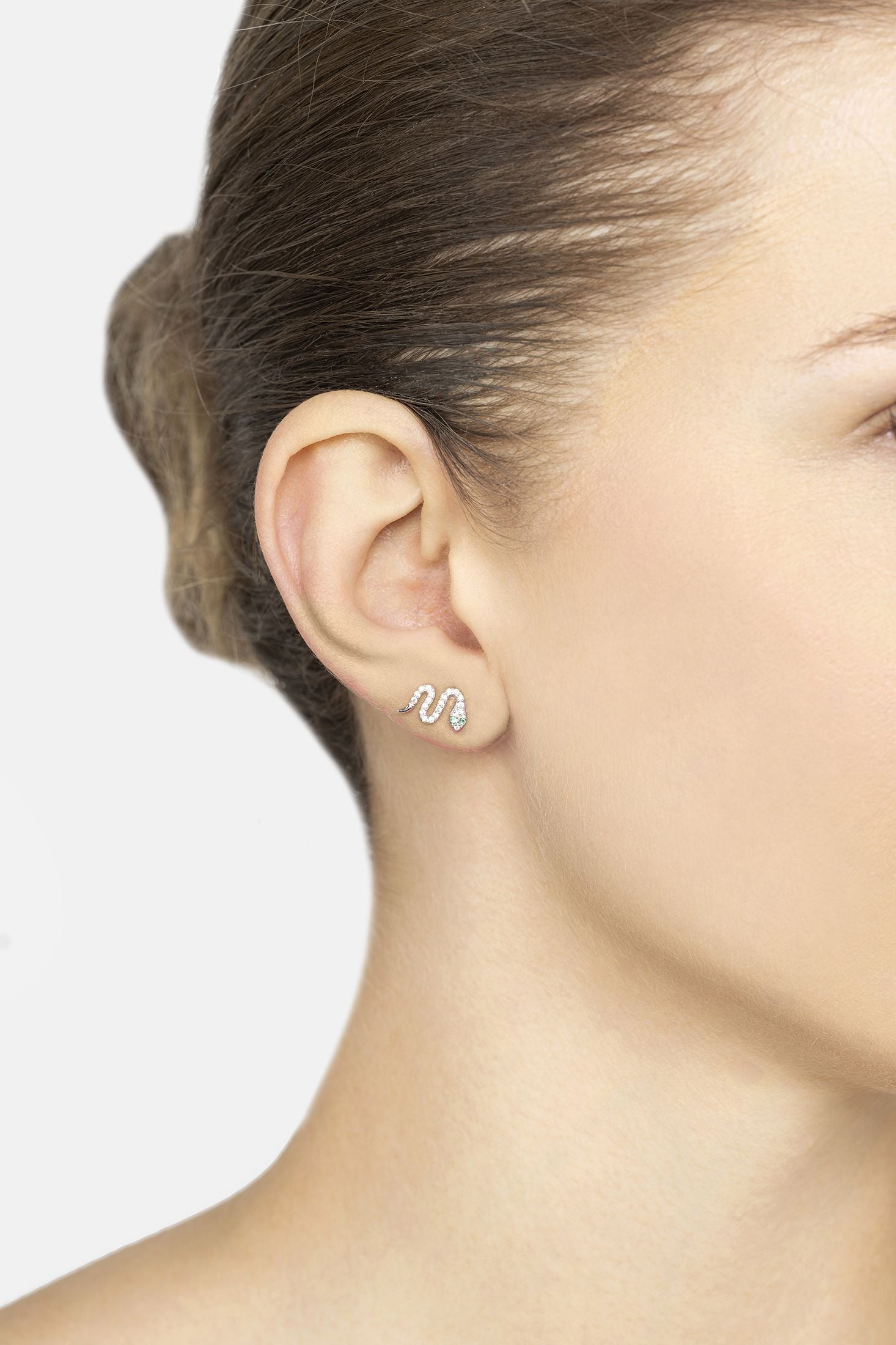 Close-up of a person wearing a snake-shaped earring on a plain background